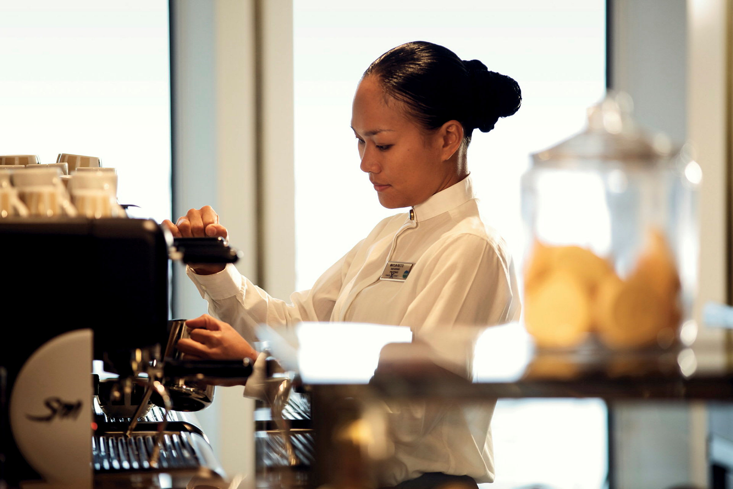 En person i uniform står ved en kaffemaskin og tilbereder drikke. (AI-generert tekst)