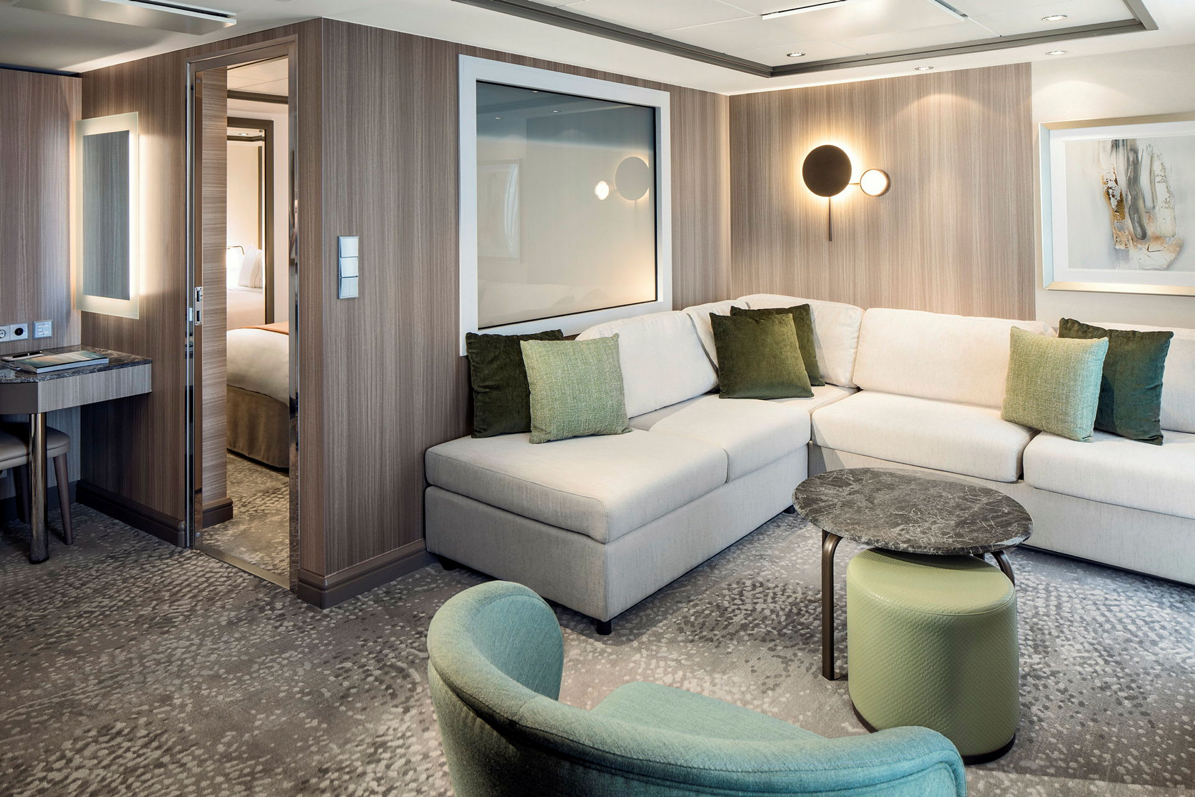 Et moderne hotellrom med en L-formet sofa, grønne puter, et lite bord og en sitteinredning. (AI-generert tekst)