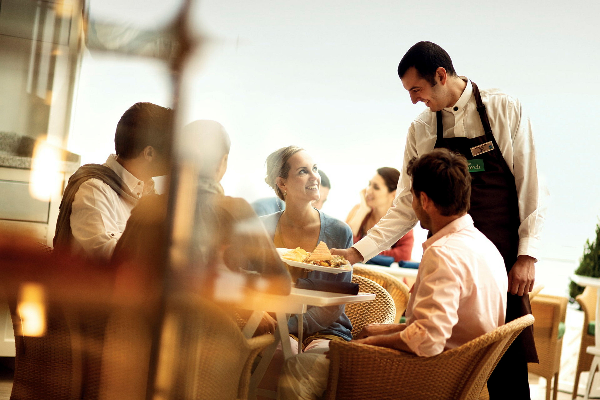 En servitør serverer mat til gjester ved et bord på en restaurant. (AI-generert tekst)