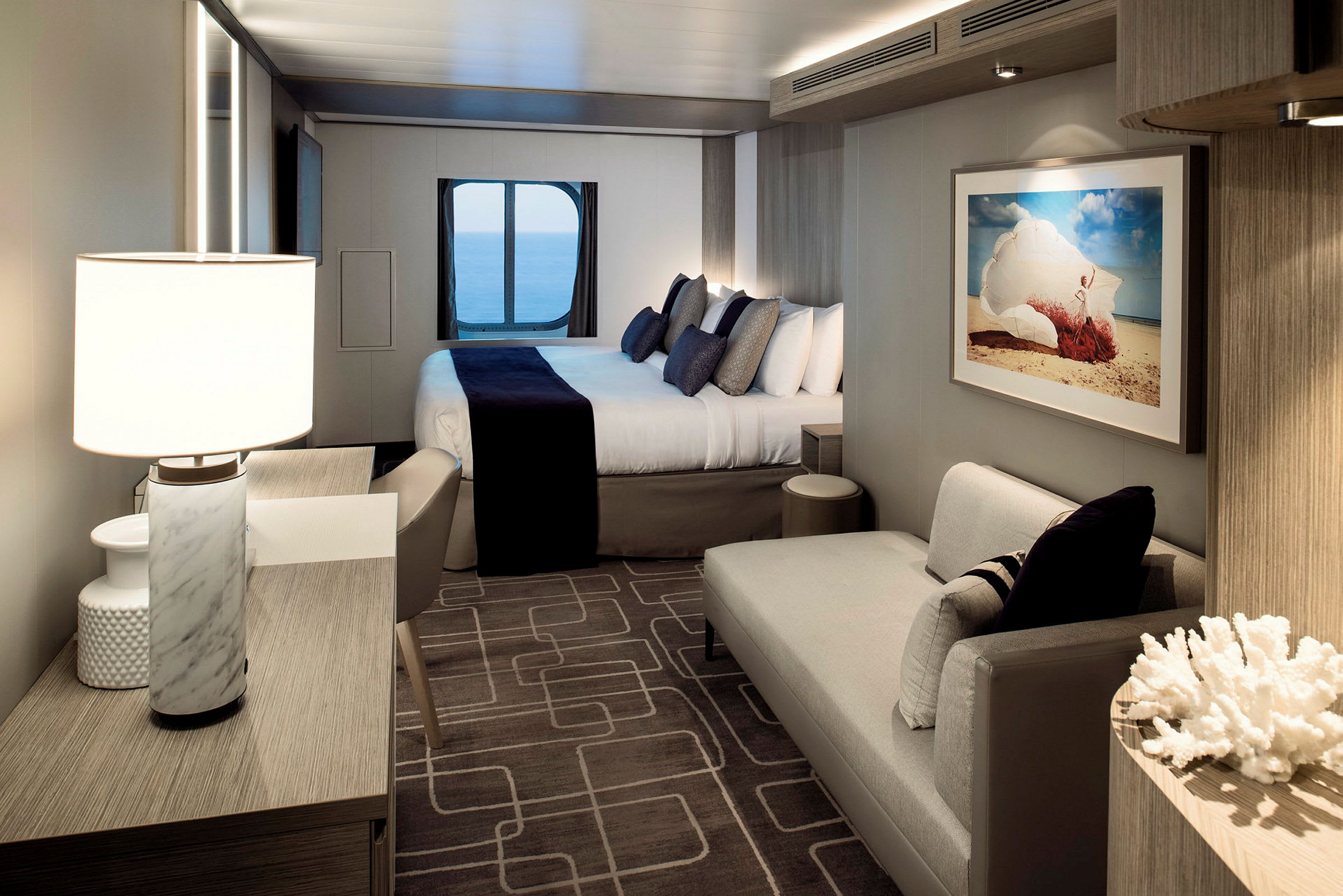 Moderne og elegant hotellrom med en dobbeltseng, sittegruppe og havutsikt gjennom et rundt vindu. (AI-generert tekst)