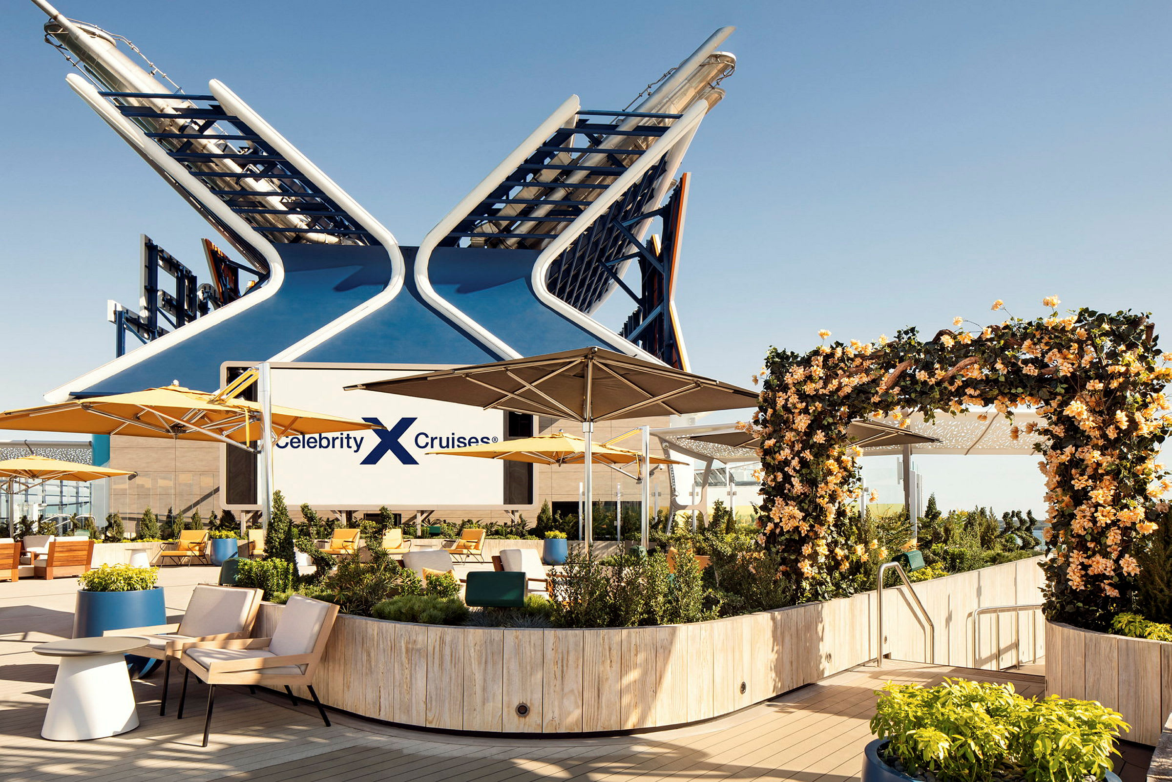Et skipsdekk med sittegrupper, gule parasoller og velstelt beplantning, med logoen 'Celebrity Cruises' synlig. (AI-generert tekst)