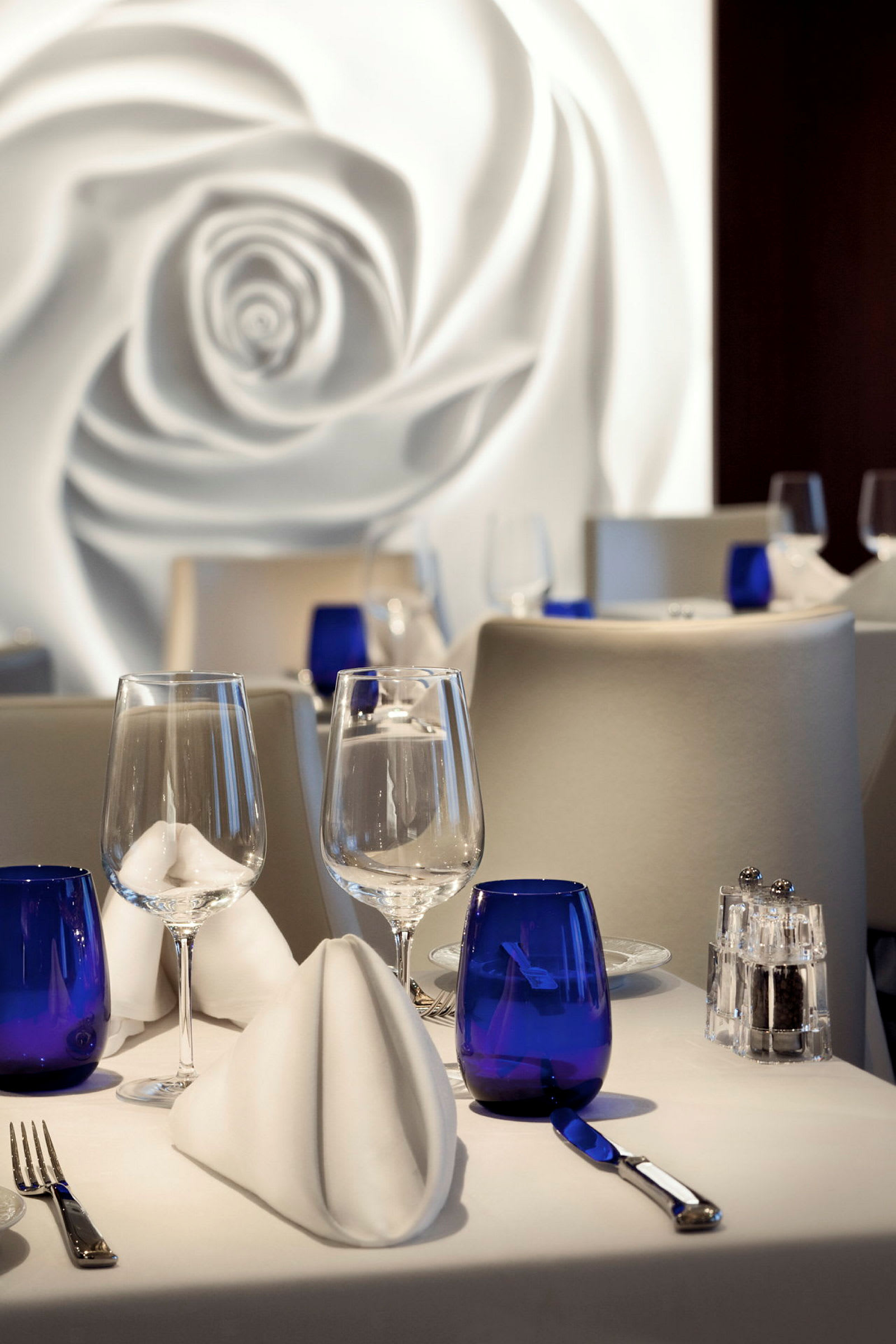 Bilde av et dekket bord i en elegant restaurant med blå glass og hvite servietter. (AI-generert tekst)