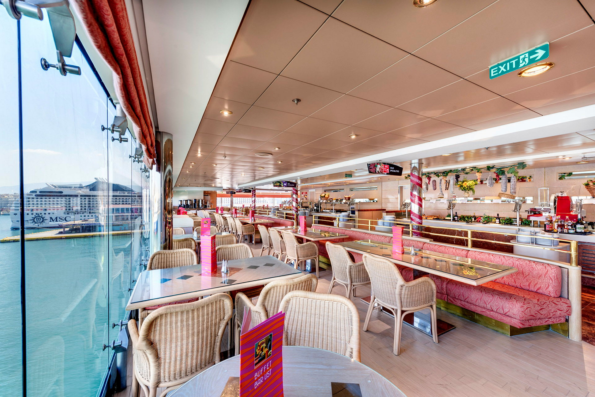 Innendørsbilde av en lys restaurant med sitteplasser og store vinduer som gir utsikt mot et skip ved en havn. (AI-generert tekst)