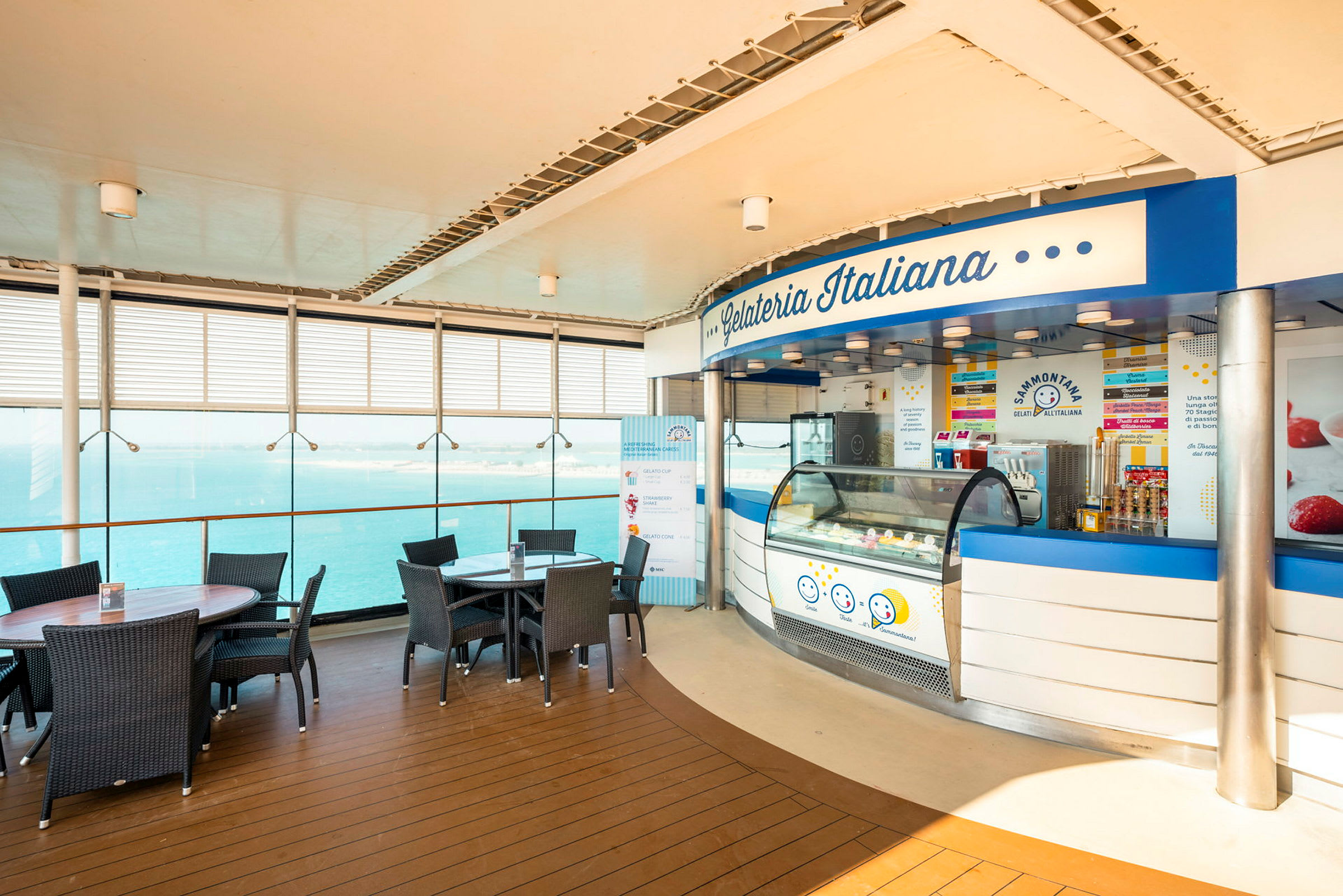 En iskiosk med navnet Gelateria Italiana beliggende ved et område med bord og stoler nær glassvinduer med utsikt over havet. (AI-generert tekst)