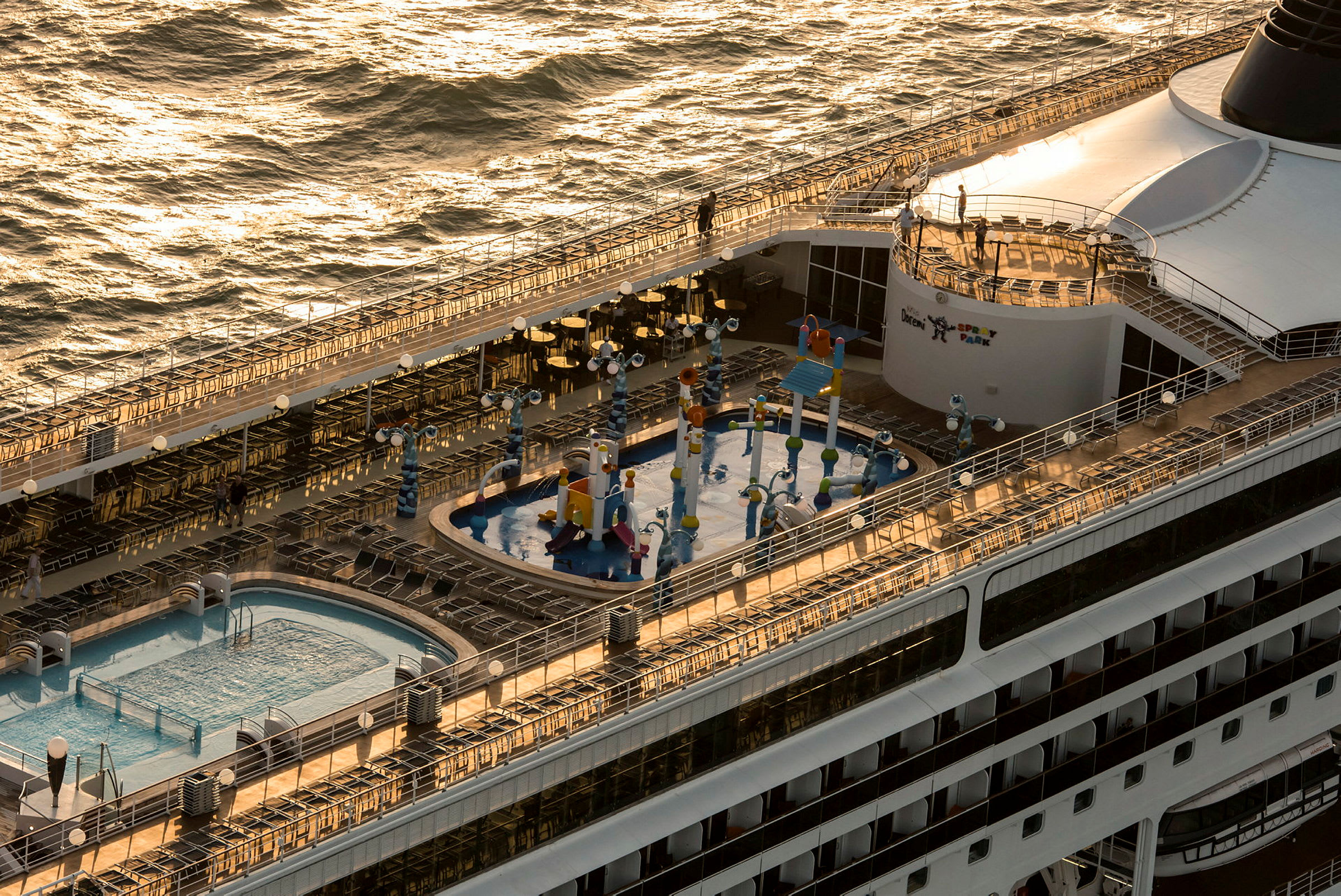 Et cruiseskip med utendørs basseng og vannlekeplass på dekk. Havet ses rundt. (AI-generert tekst)