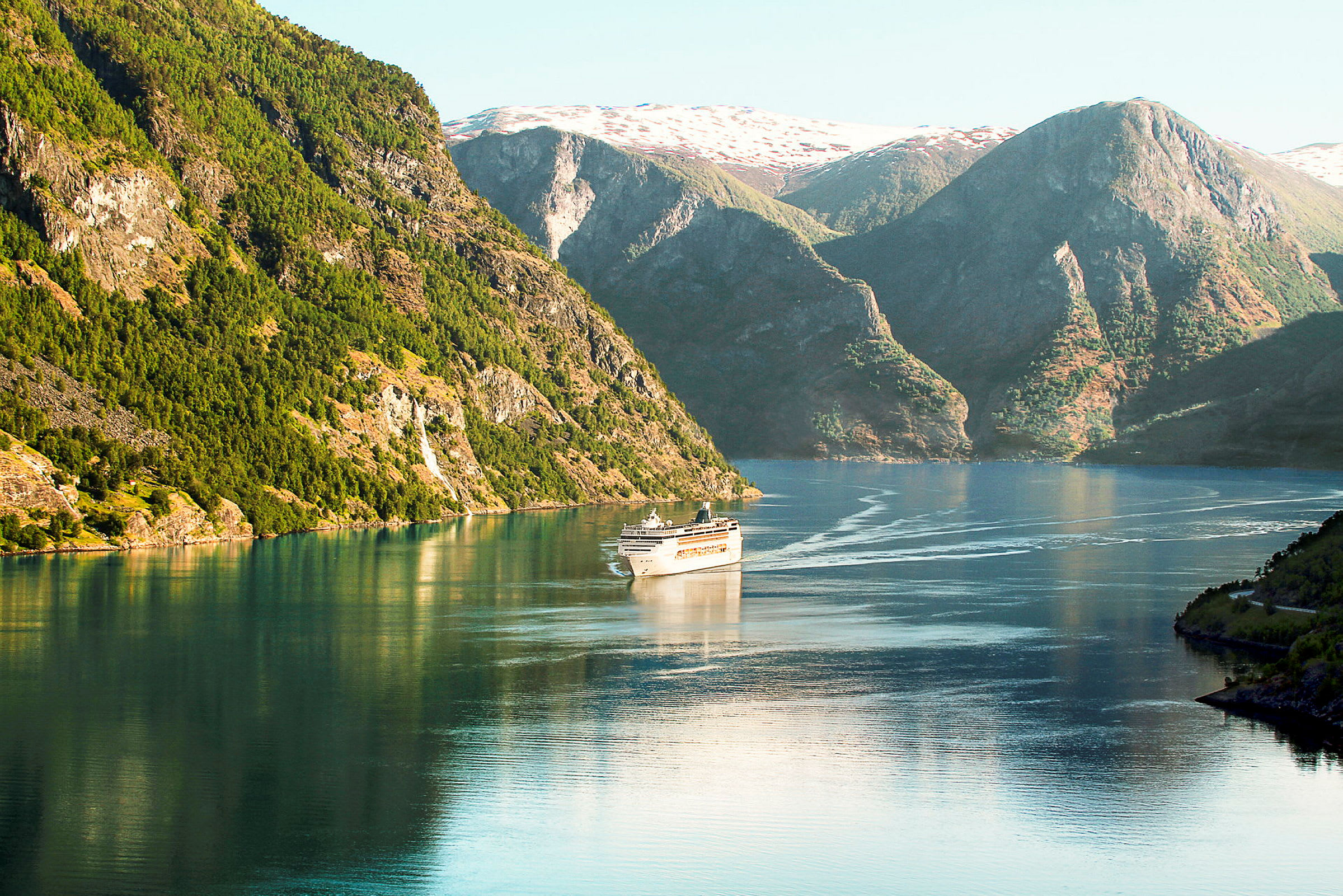 Bilde av et cruiseskip som seiler gjennom en fjord med høye fjellsider og klart vann. (AI-generert tekst)
