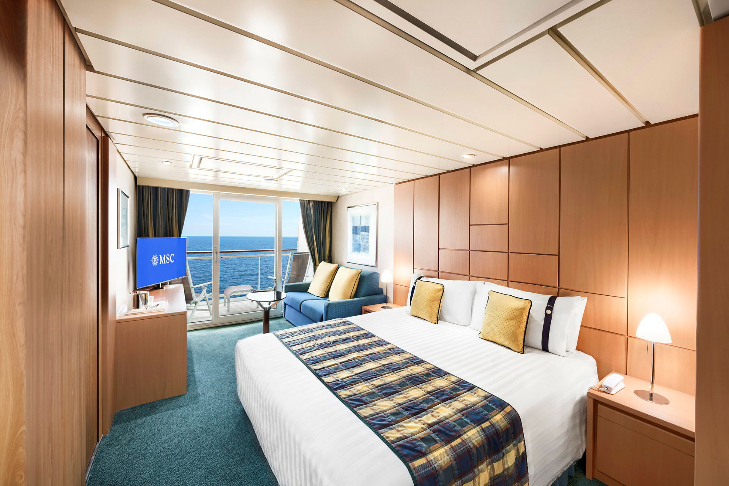 Bilde av et romslig og elegant innredet hotellrom med stor seng, sitteområde og havutsikt gjennom glassdører. (AI-generert tekst)