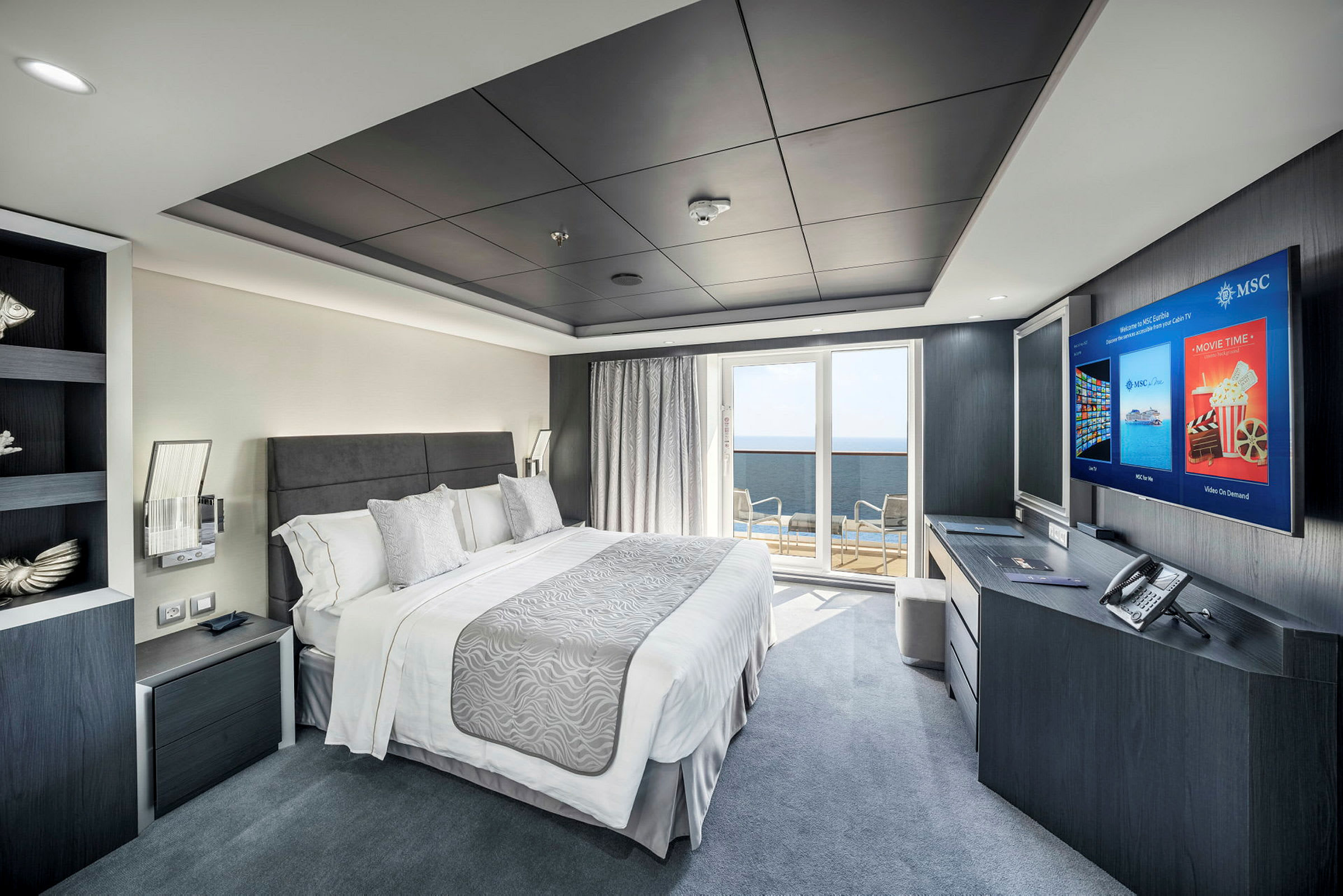 Et moderne hotellrom med en dobbeltseng, skrivebord med TV, balkong med utsikt og elegant innredning. (AI-generert tekst)