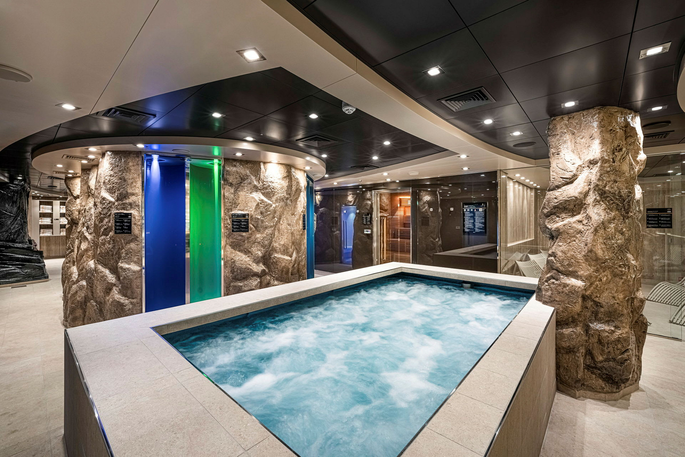 Et spaområde med en jacuzzi omgitt av steinlignende søyler og fargede glassdører. (AI-generert tekst)