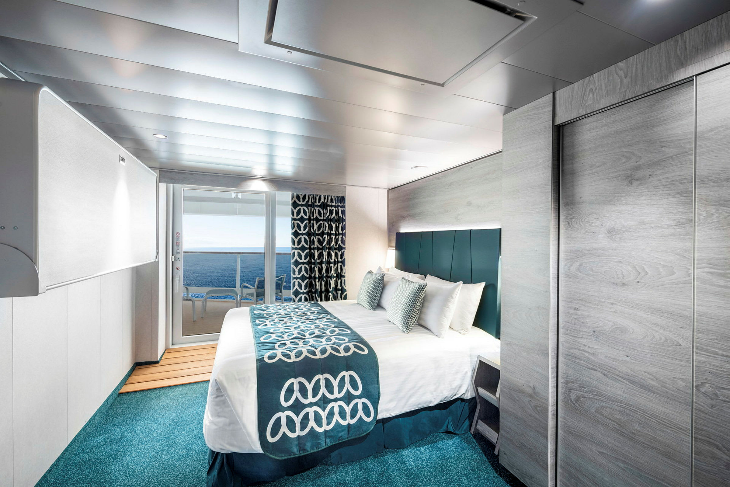 Et moderne innredet hotellrom med en stor seng, utsikt mot havet gjennom glassdører, og smakfulle blå og hvite detaljer i interiøret. (AI-generert tekst)