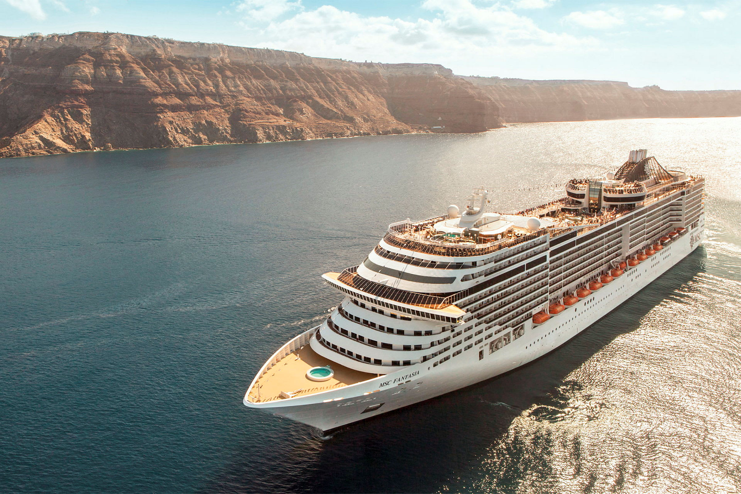 Et cruiseskip seiler i en havbukt med høye klipper i bakgrunnen. (AI-generert tekst)