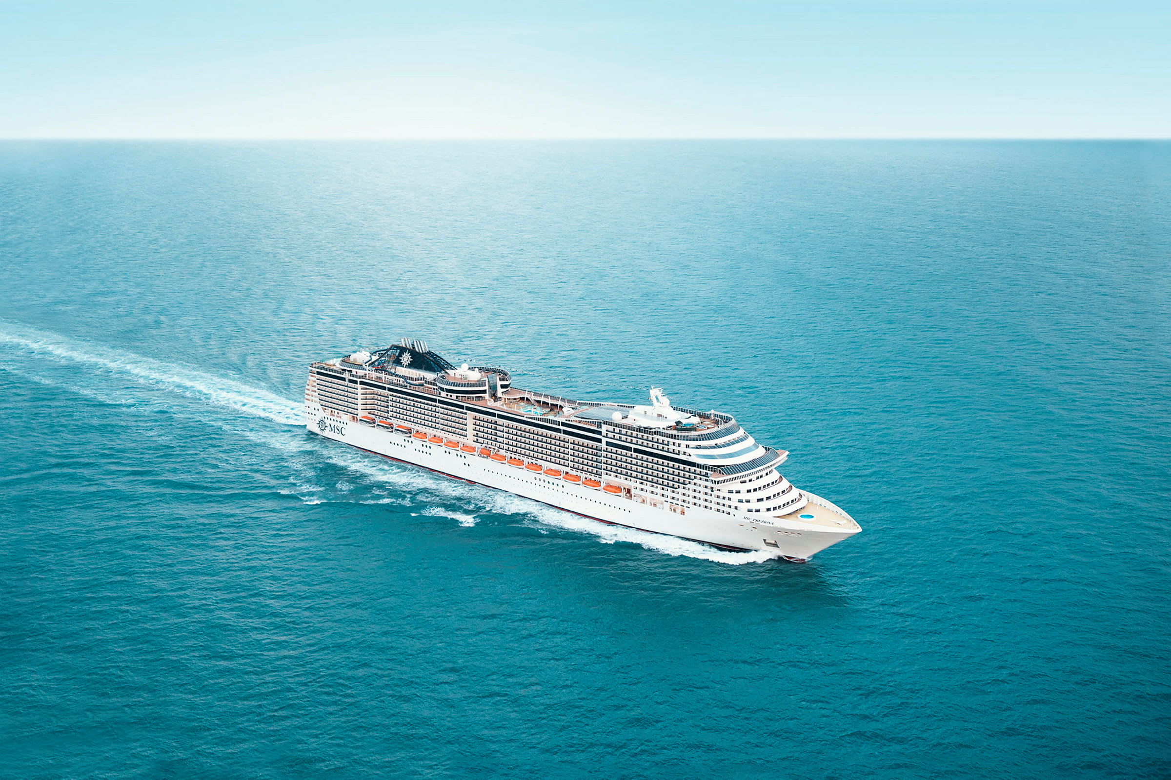 Et stort cruiseskip med hvite og blå detaljer seiler på et rolig blått hav under en klar himmel. (AI-generert tekst)