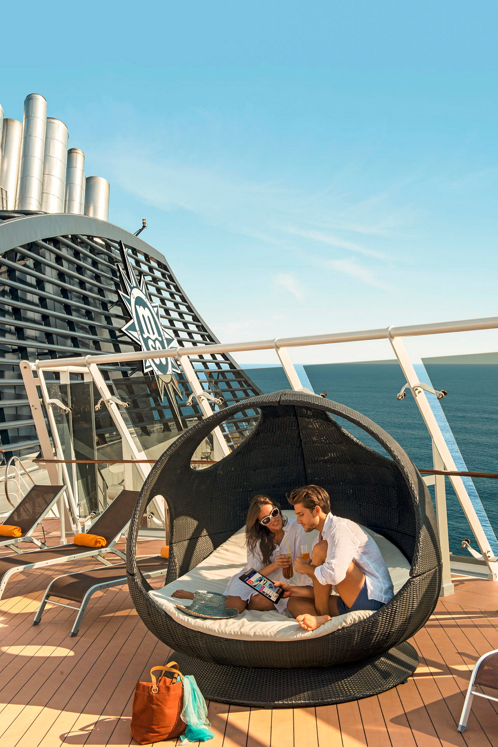 Personer sitter i en rund liggestol med havet i bakgrunnen på et cruiseskip. (AI-generert tekst)