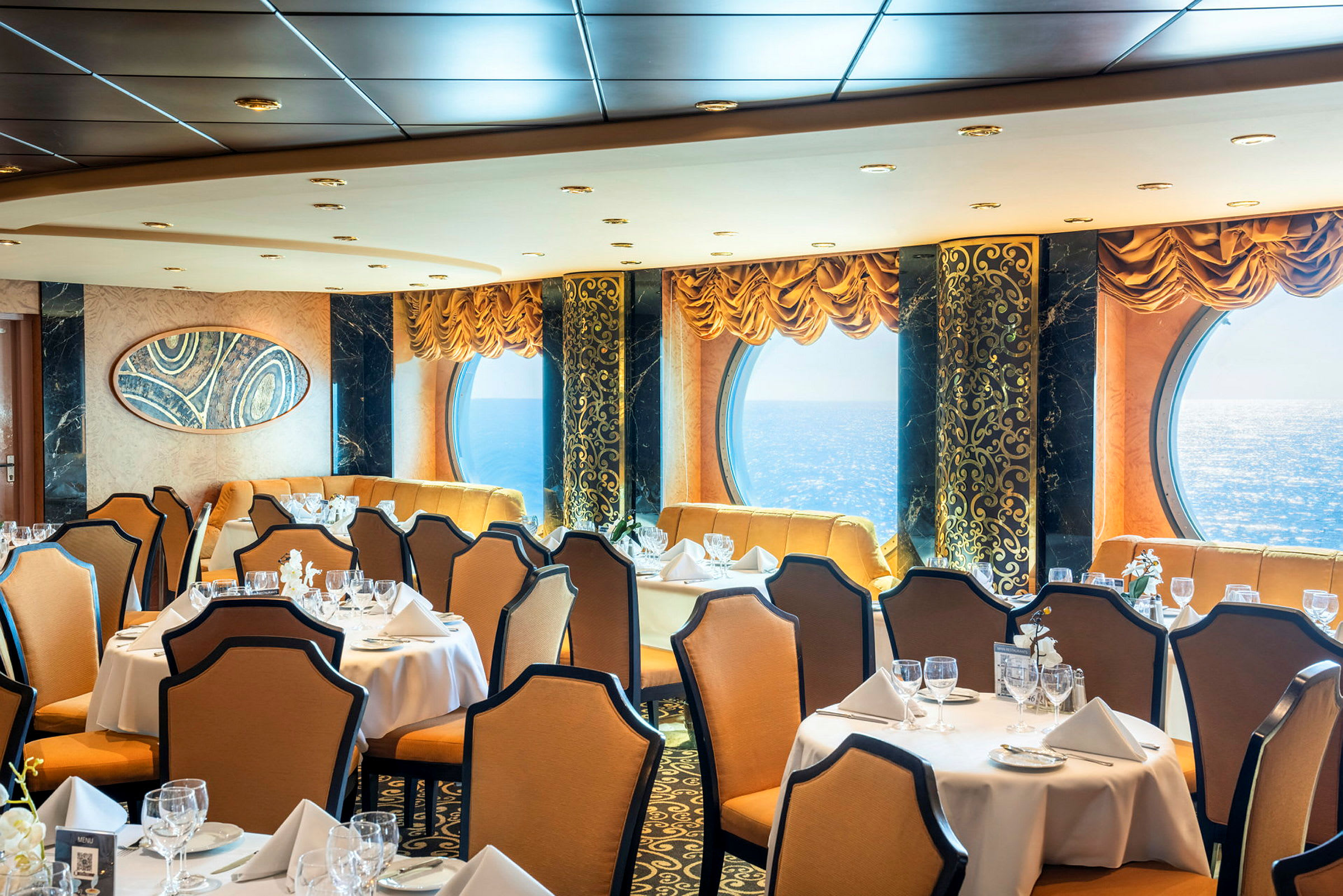 En elegant restaurant med dekkede bord, beige stoler og store vinduer med havutsikt. (AI-generert tekst)