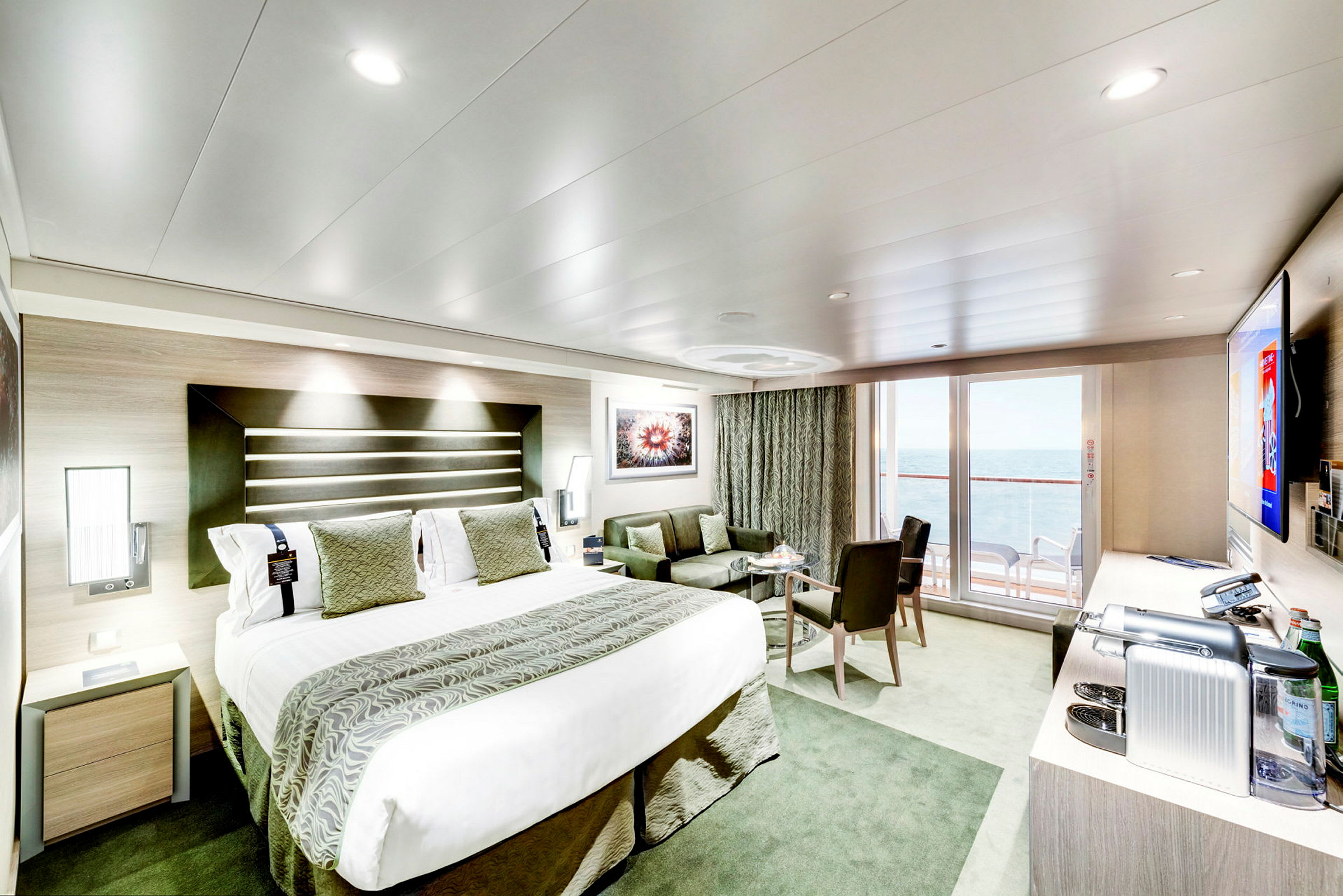 Moderne hotellrom med stor seng, sittegruppe og balkong med havutsikt. (AI-generert tekst)