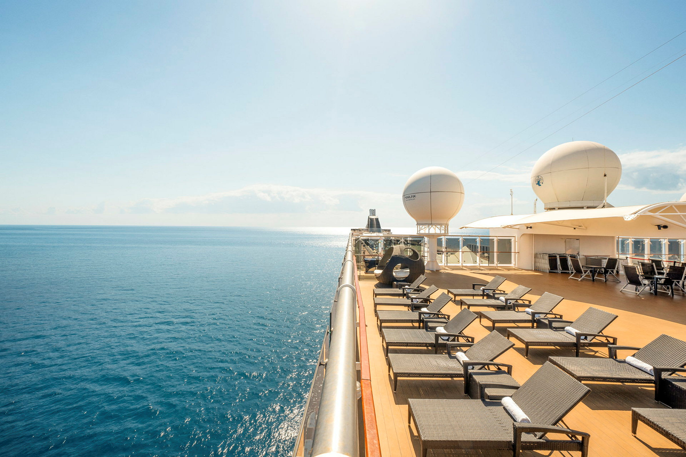 Solstoler på dekk på et cruiseskip med havet og klar blå himmel i bakgrunnen. (AI-generert tekst)