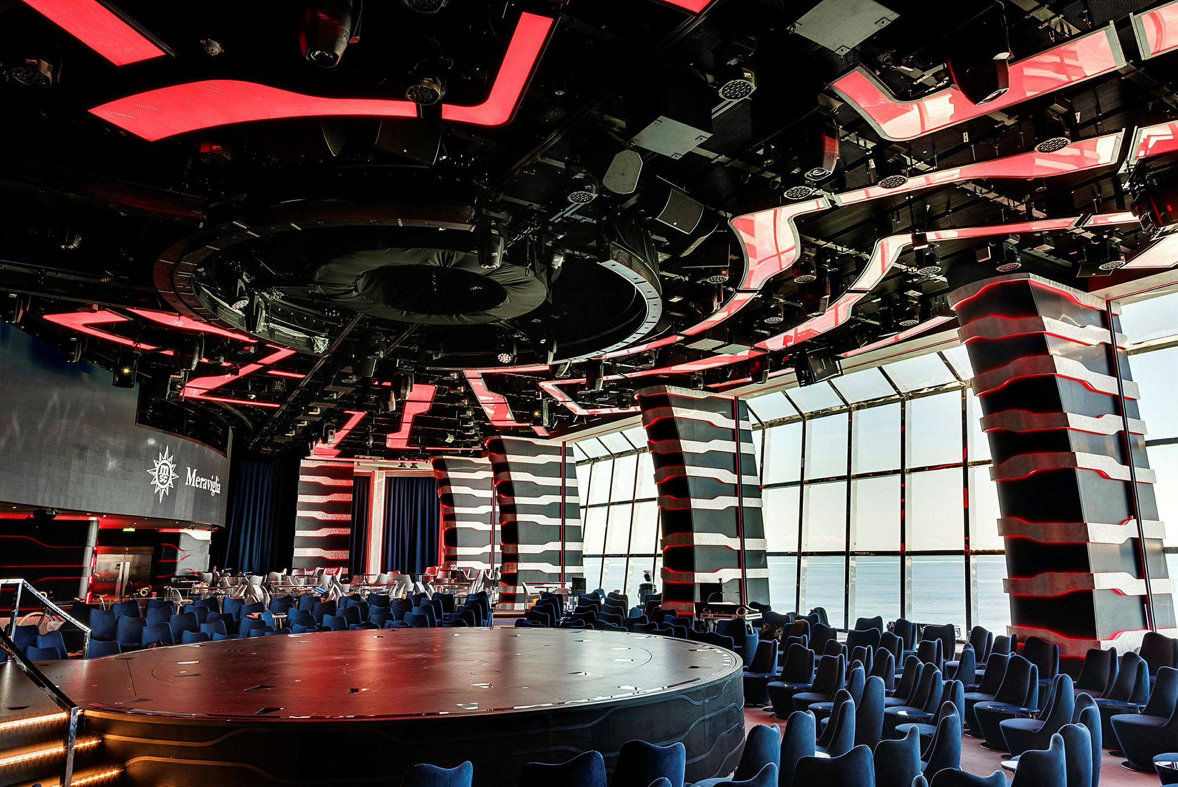 Et moderne auditorium med rød og svart tak, sitteplasser og store vinduer. (AI-generert tekst)