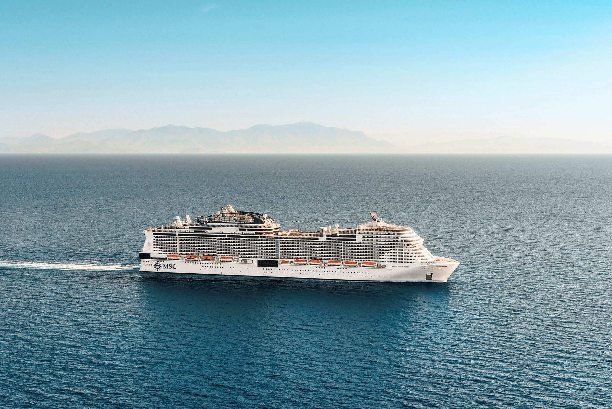 Et cruiseskip på havet med kystlinje og fjell i bakgrunnen. (AI-generert tekst)