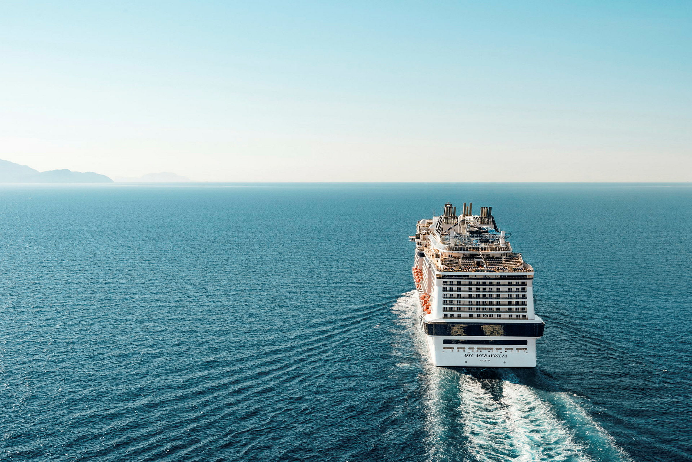 Et cruiseskip på åpent hav med land synlig i bakgrunnen. (AI-generert tekst)