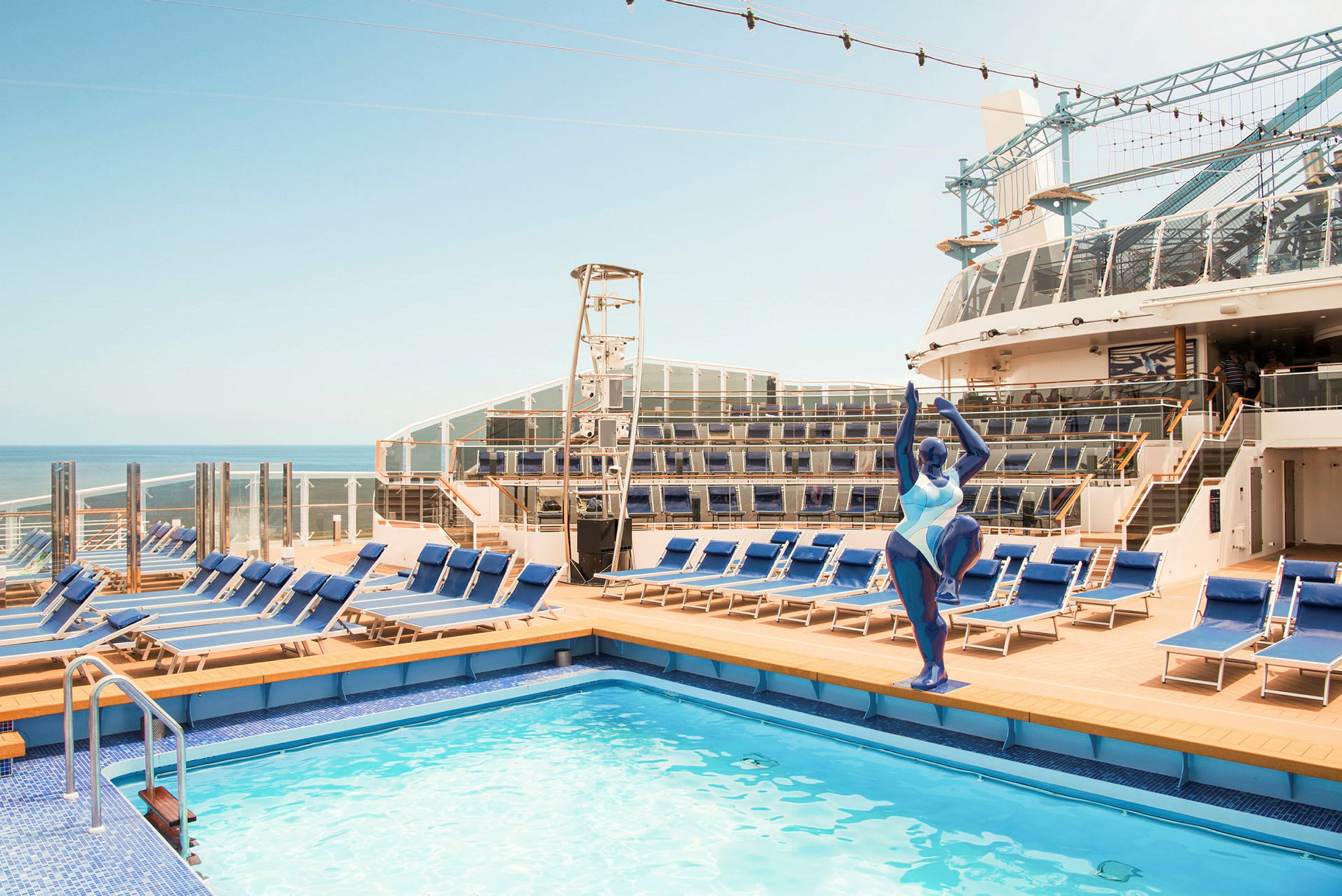 Bassengområde på cruiseskip med solsenger og skulptur i forgrunnen. (AI-generert tekst)