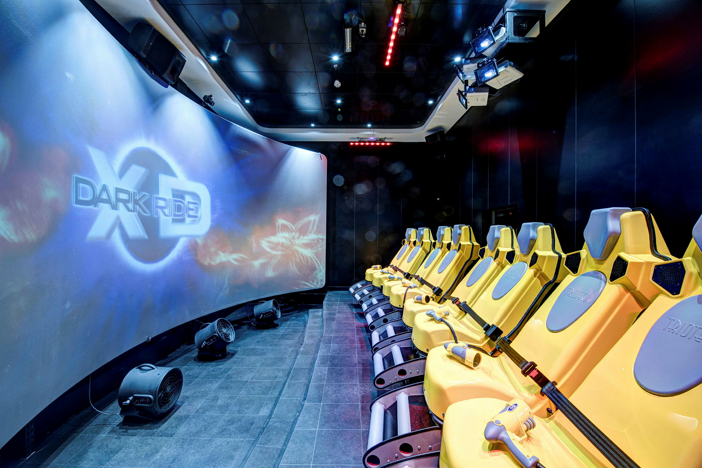 Rad med gule seter foran en stor buet skjerm med teksten "XD Dark Ride". (AI-generert tekst)