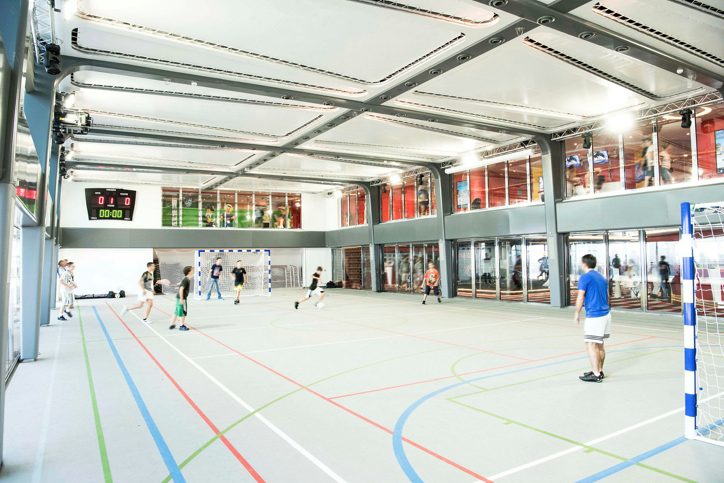 En innendørs sportshall der folk spiller fotball. (AI-generert tekst)