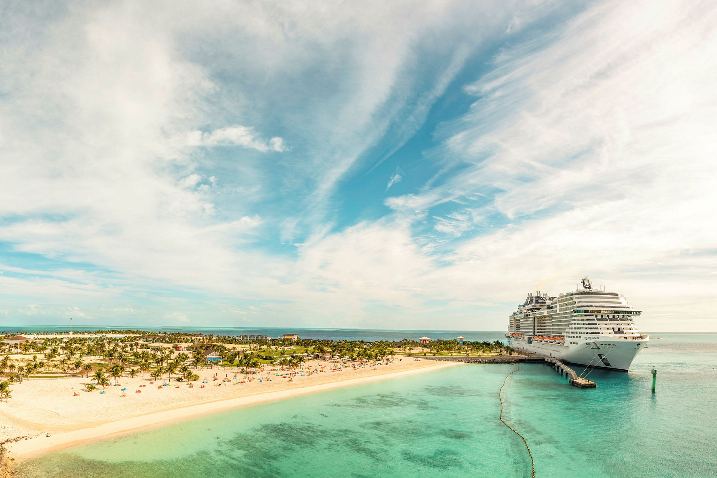 Et stort cruiseskip ligger ved en kai nær en sandstrand med palmer. (AI-generert tekst)