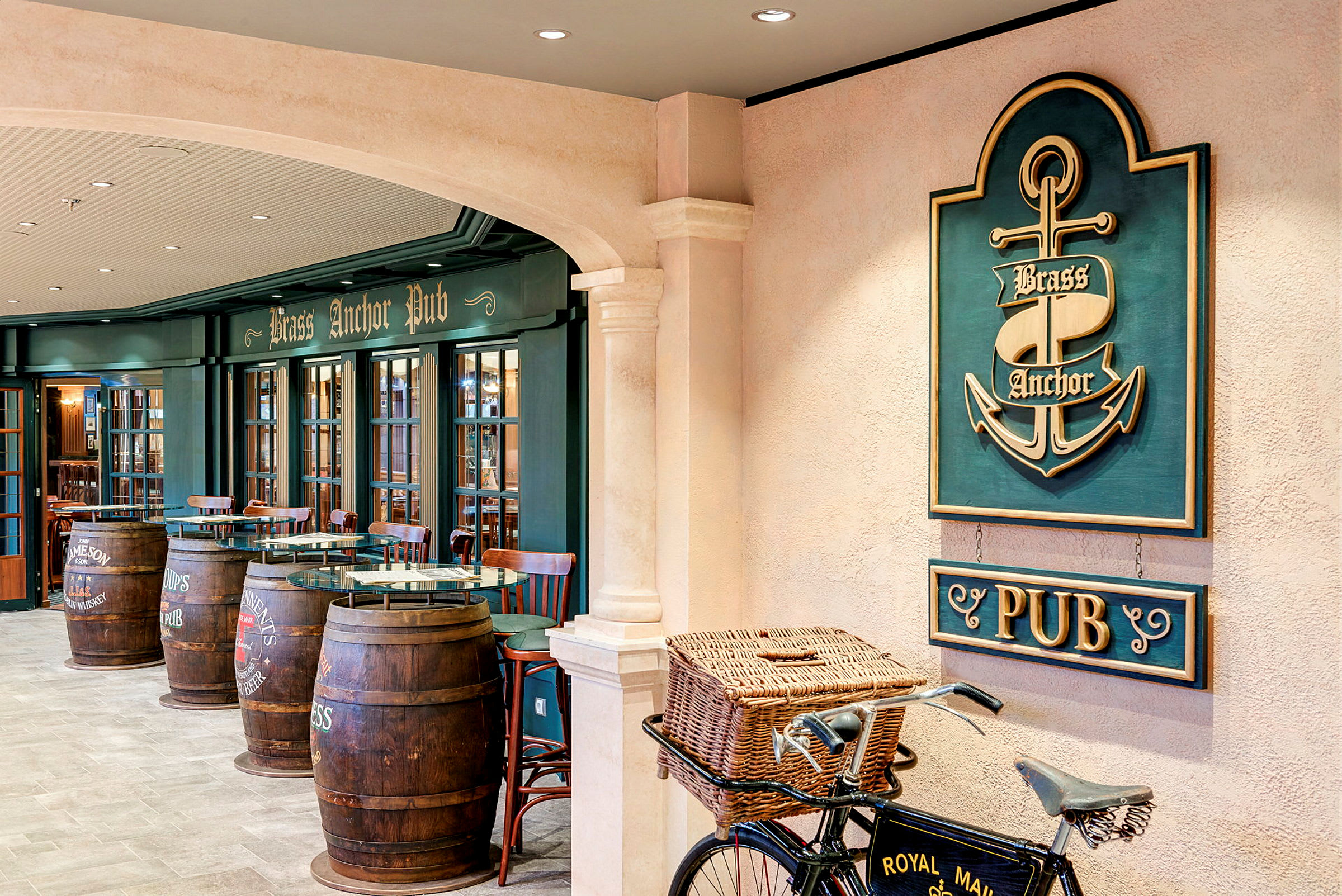 Interiør av en pub med et skilt som sier 'Brass Anchor Pub', tremøbler og tønner som brukes som bord, samt en sykkel med en kurv foran. (AI-generert tekst)