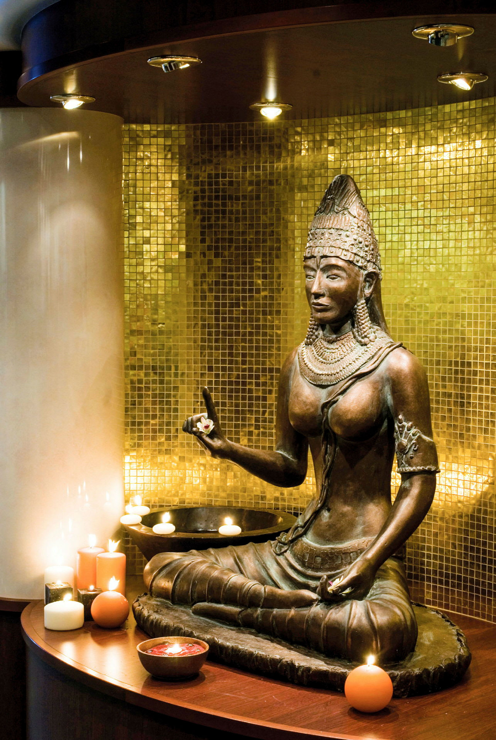 Statue av en buddhistisk figur foran en gyllen mosaikkvegg omgitt av tente lys. (AI-generert tekst)