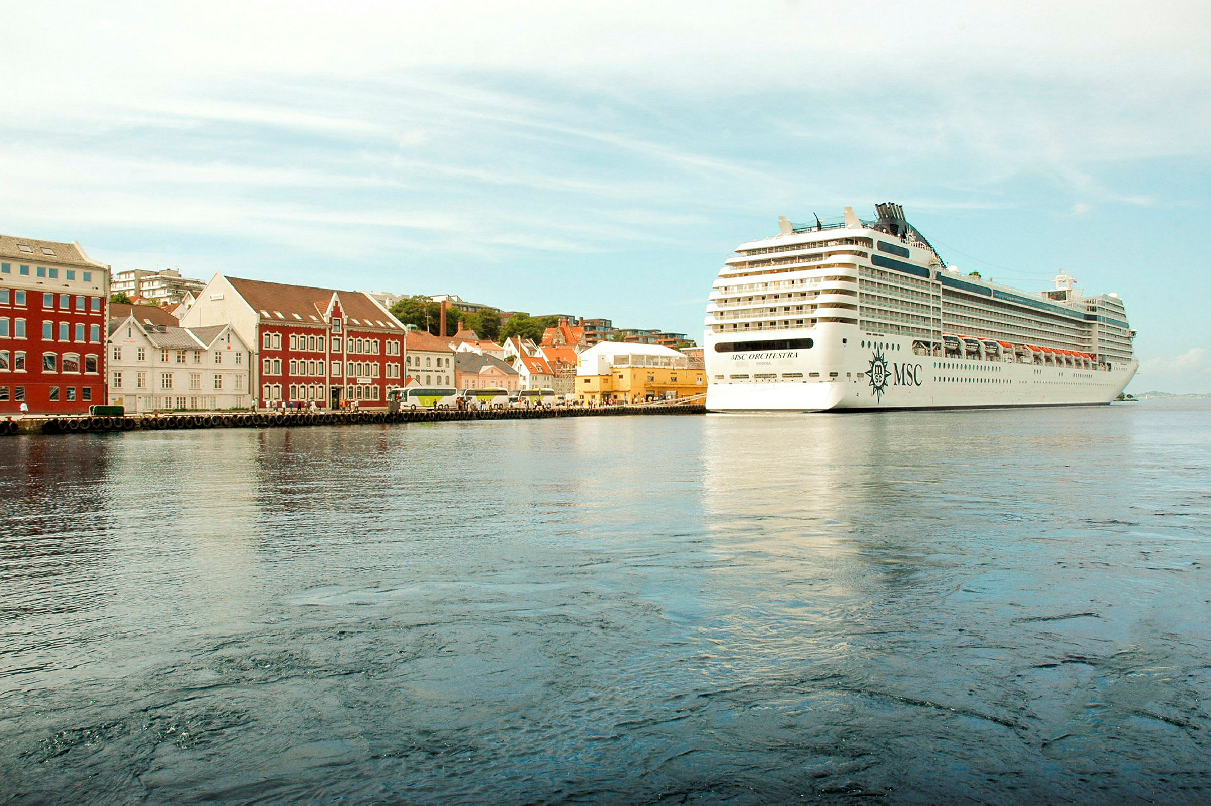 Et stort cruiseskip ligger ved kai ved siden av bygninger i forskjellige farger. (AI-generert tekst)