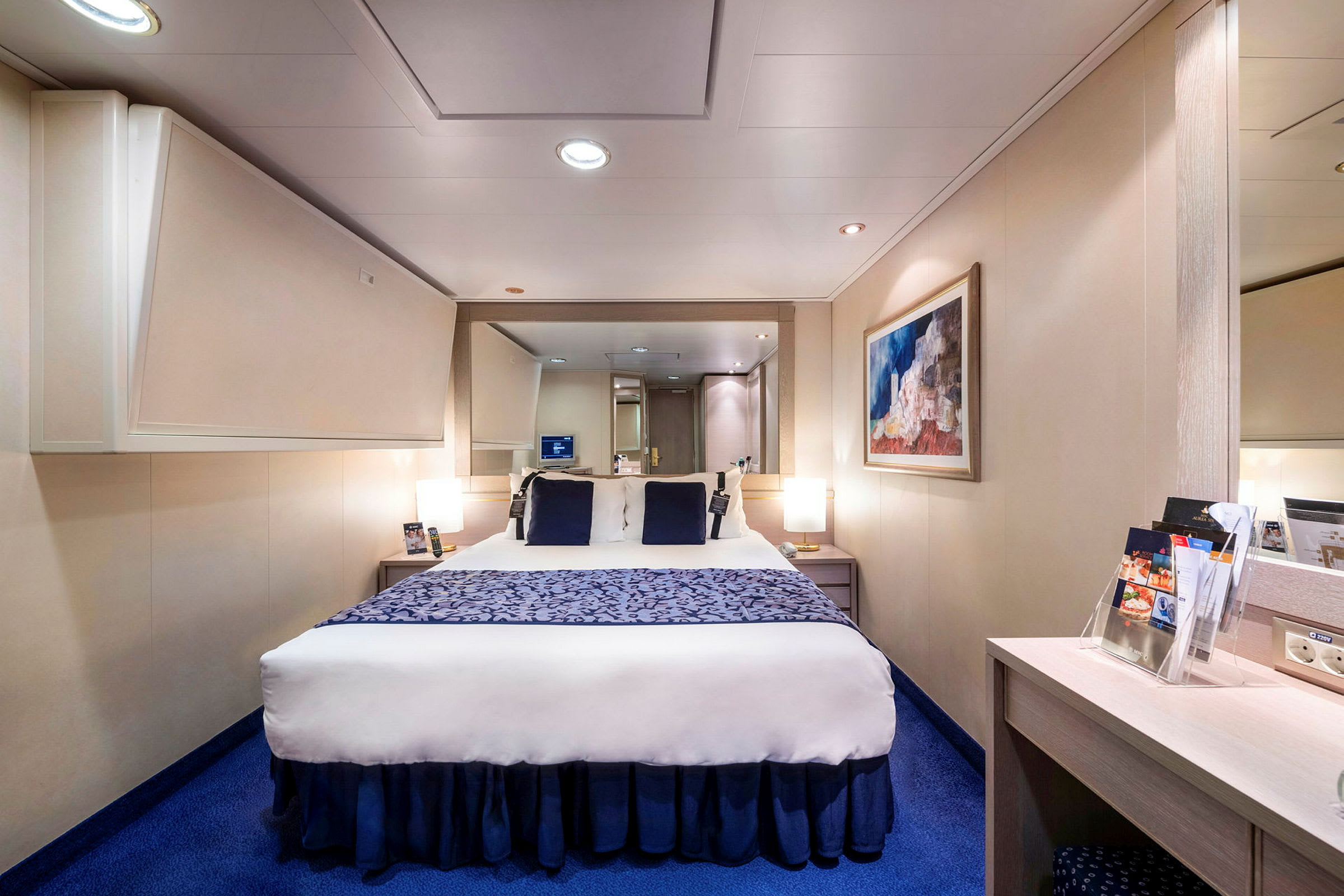 Bilde av et moderne hotellrom med en dobbeltseng, blått teppe og veggdekor. (AI-generert tekst)