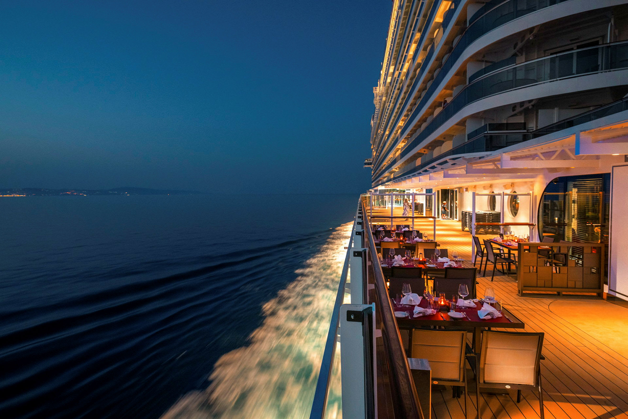 Bilde av et cruiseskip om natten med opplyste bord på dekk og havet ved siden av. (AI-generert tekst)