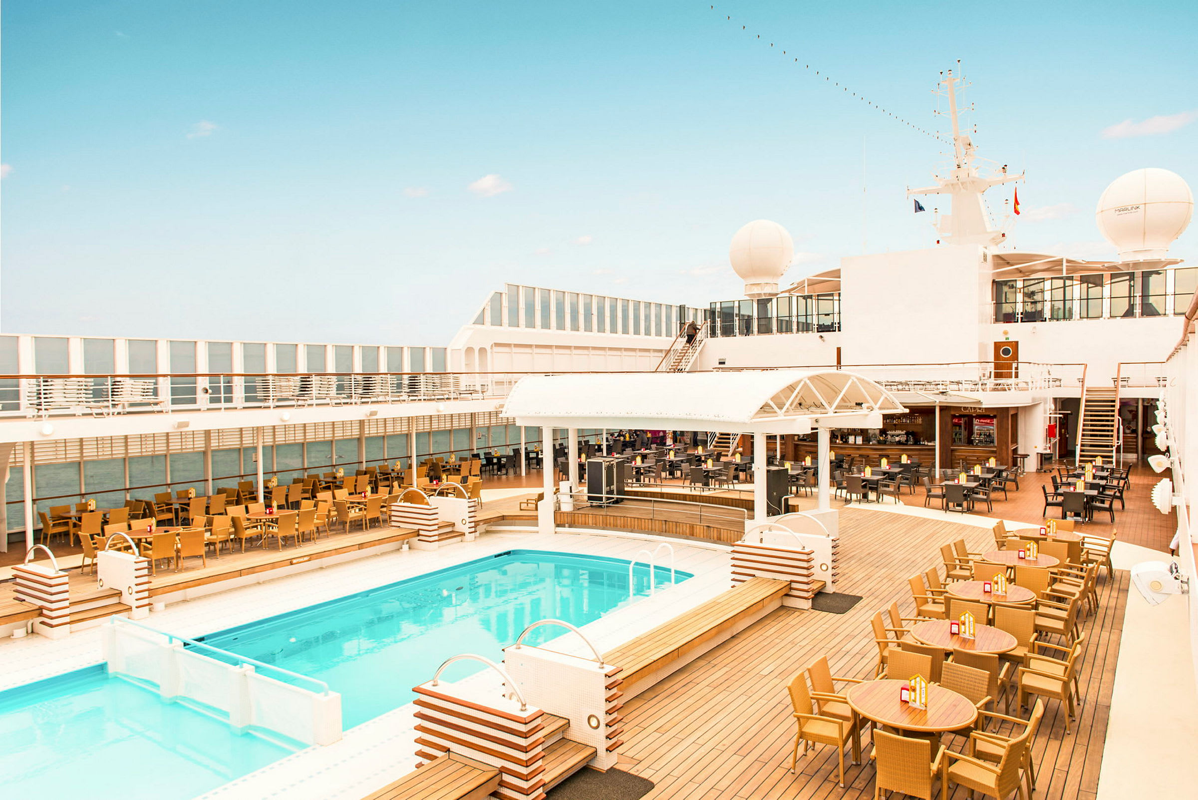 Et bilde av et basseng og utendørs servering på et cruiseskip med klar himmel. (AI-generert tekst)