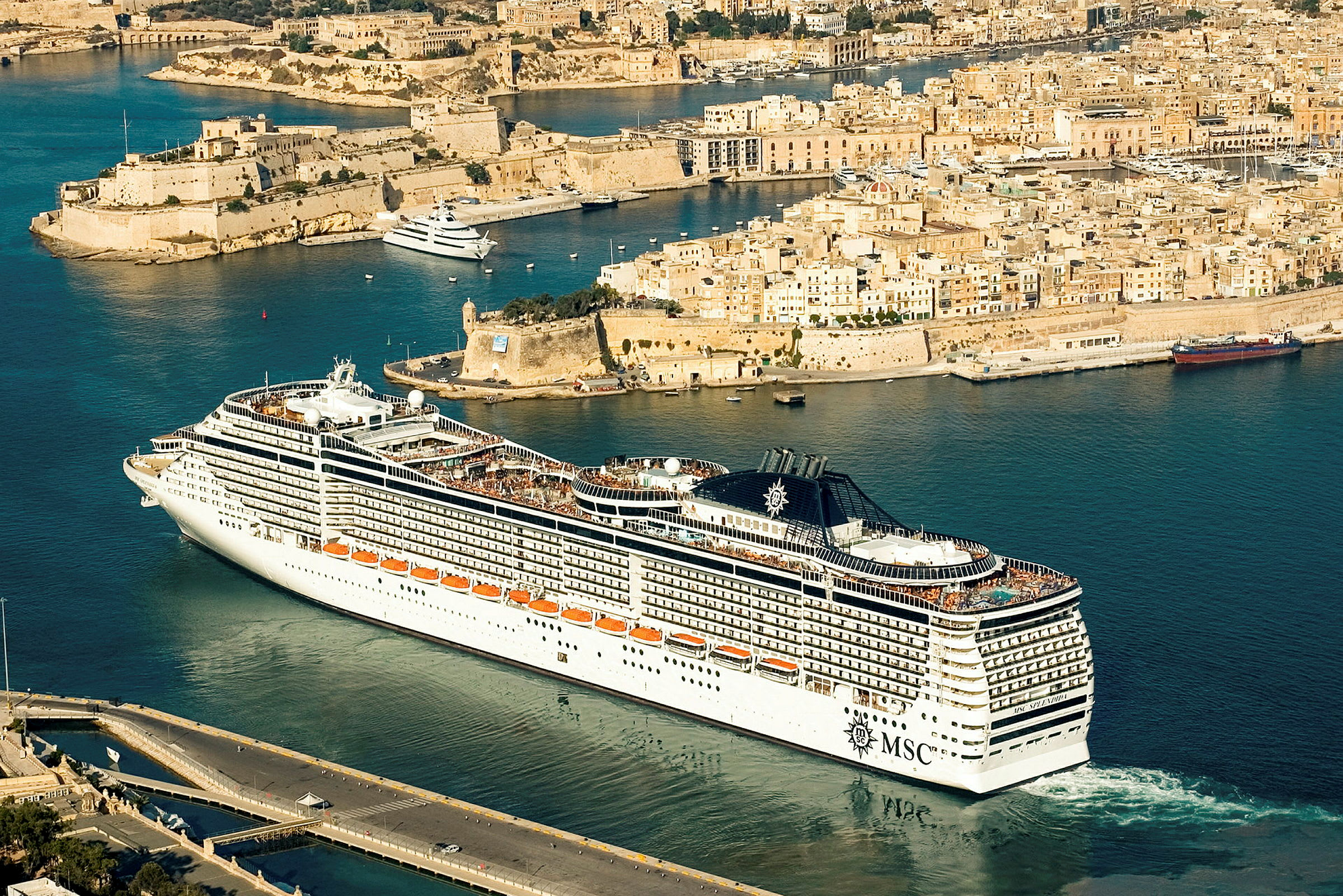 Et stort cruiseskip i en havn med eldre bygninger i bakgrunnen. (AI-generert tekst)