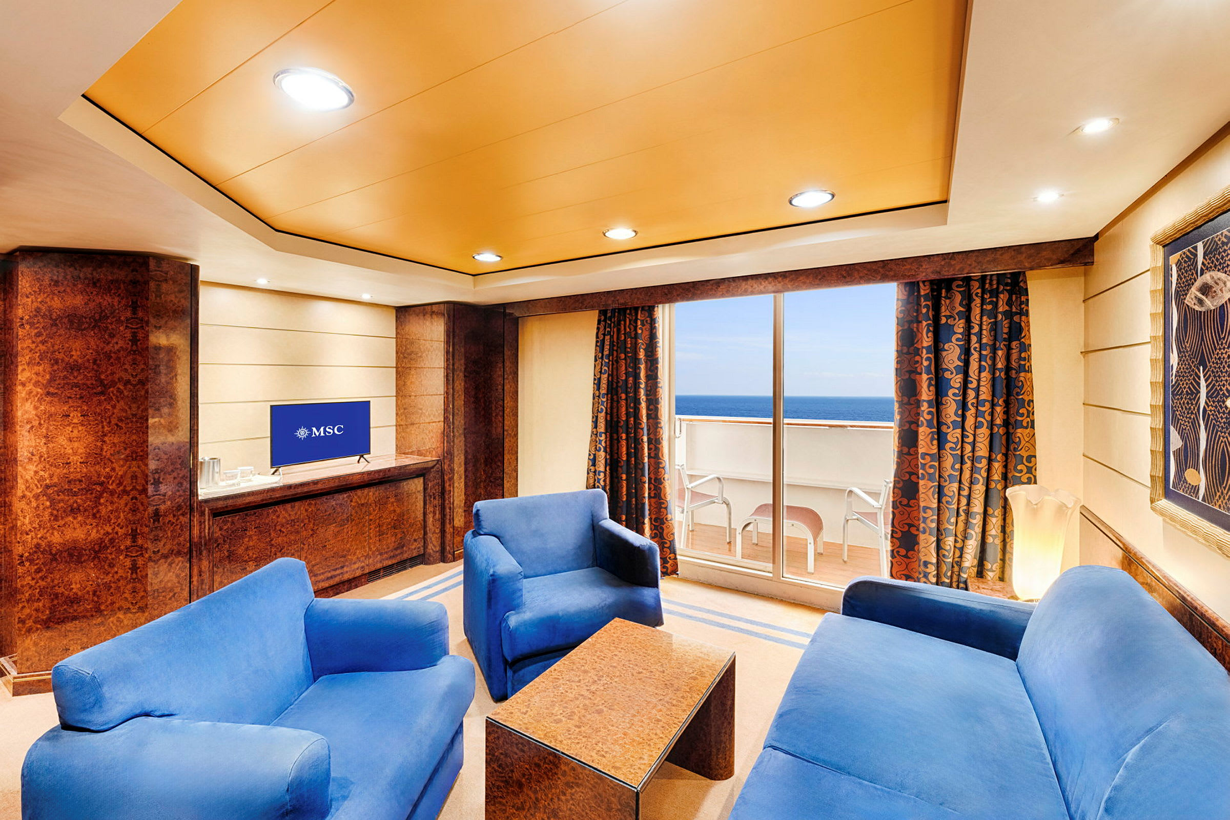 En stue med blå sofaer, et salongbord, en TV og en balkong med utsikt over havet. (AI-generert tekst)