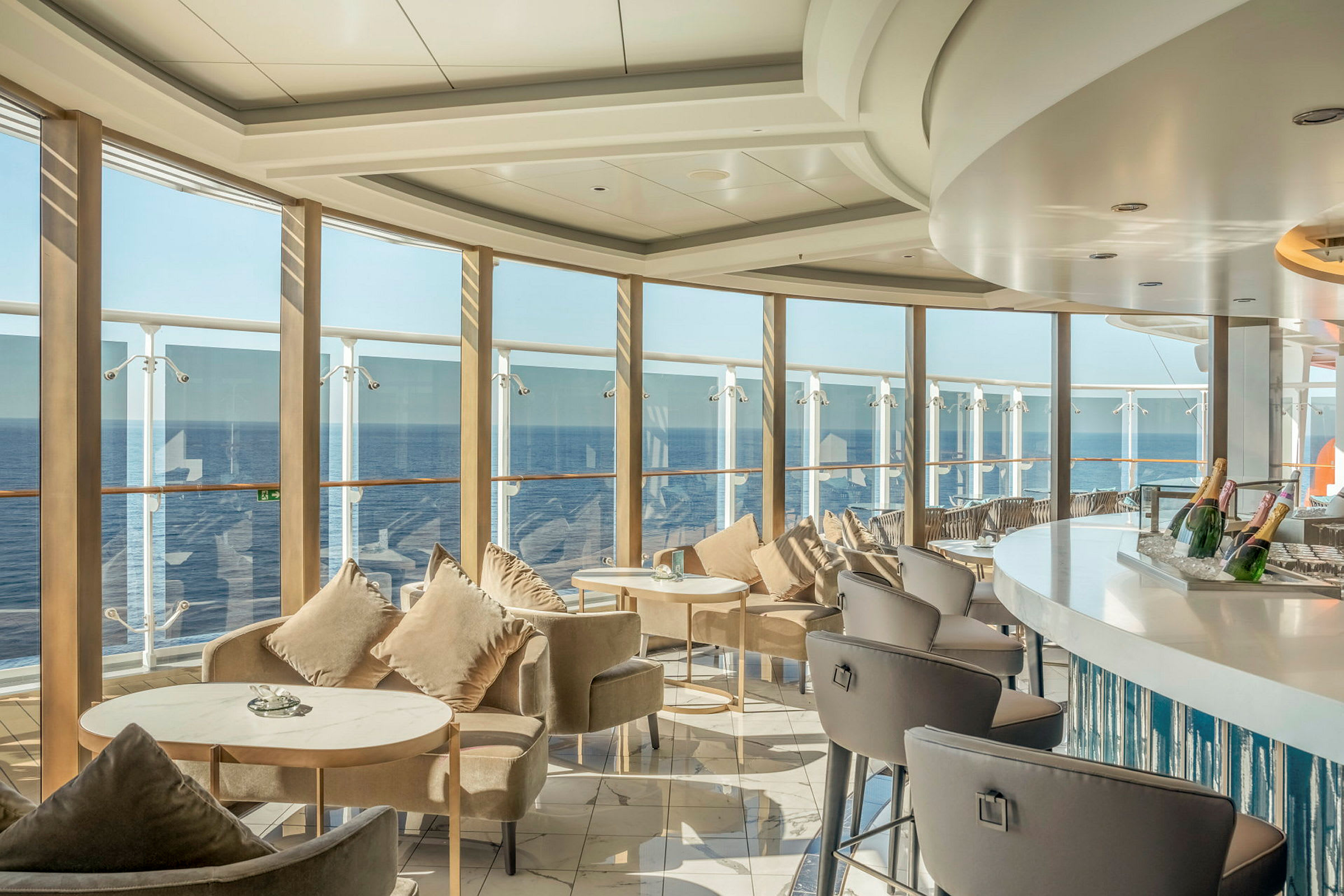 En elegant salong med sitteplasser og bord ved store vinduer med utsikt over havet. (AI-generert tekst)