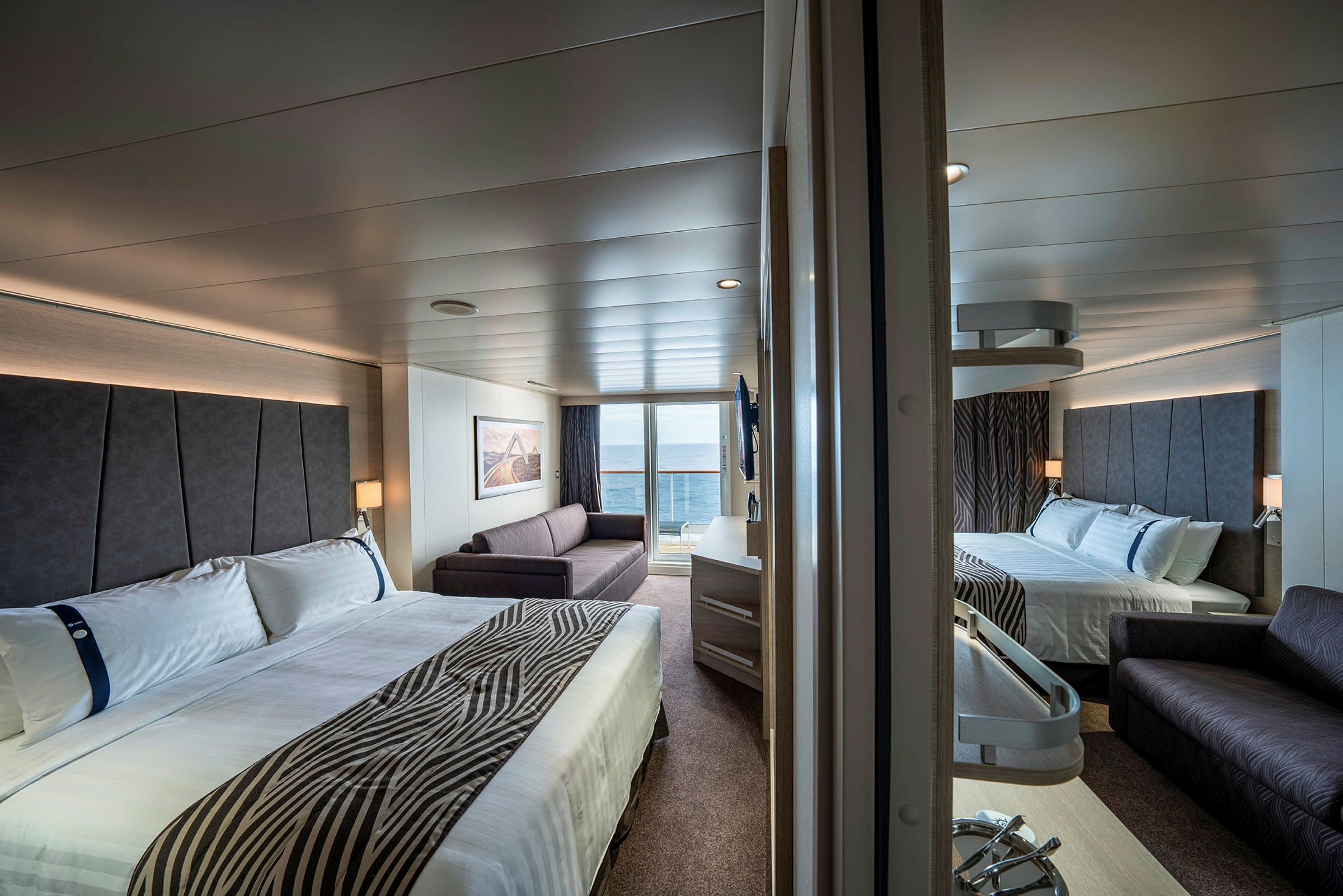 To senger og en sofa i et moderne hotellrom med havutsikt. (AI-generert tekst)