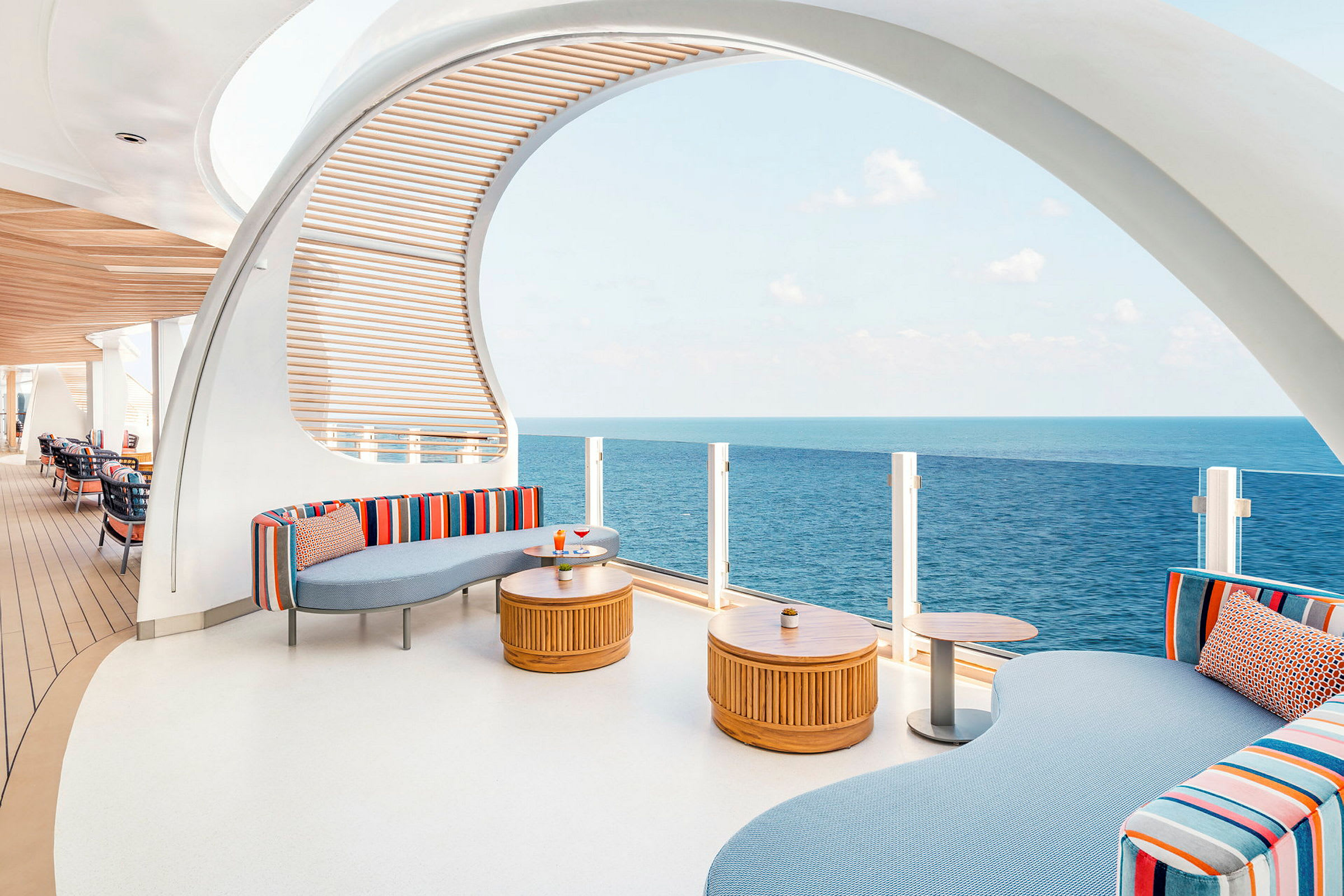En moderne lounge med fargerike sofaer, trebord og utsikt over havet. (AI-generert tekst)