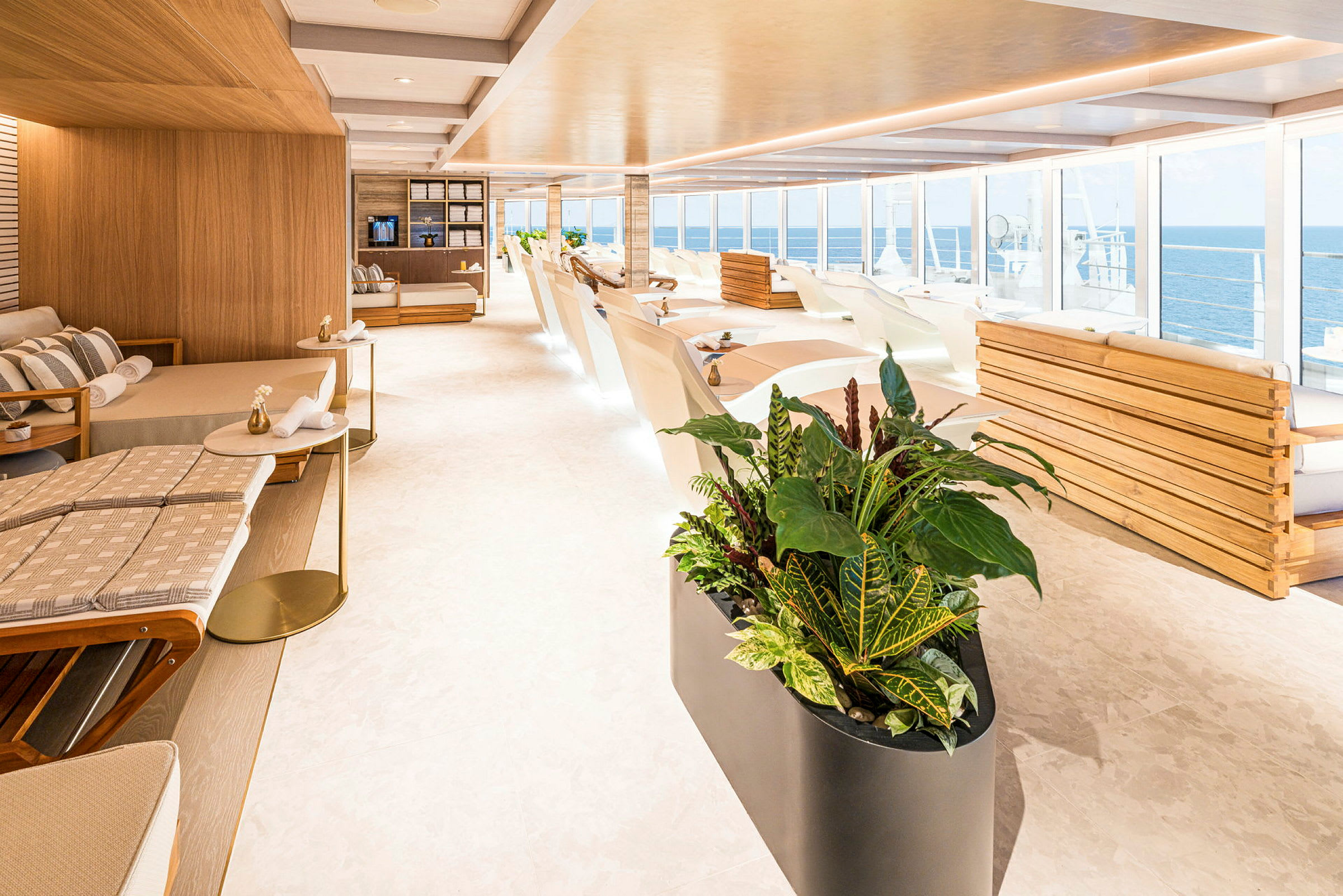 Lyst og moderne lounge med liggestoler, sofaer og store vinduer med utsikt over havet. Planter i forgrunnen. (AI-generert tekst)