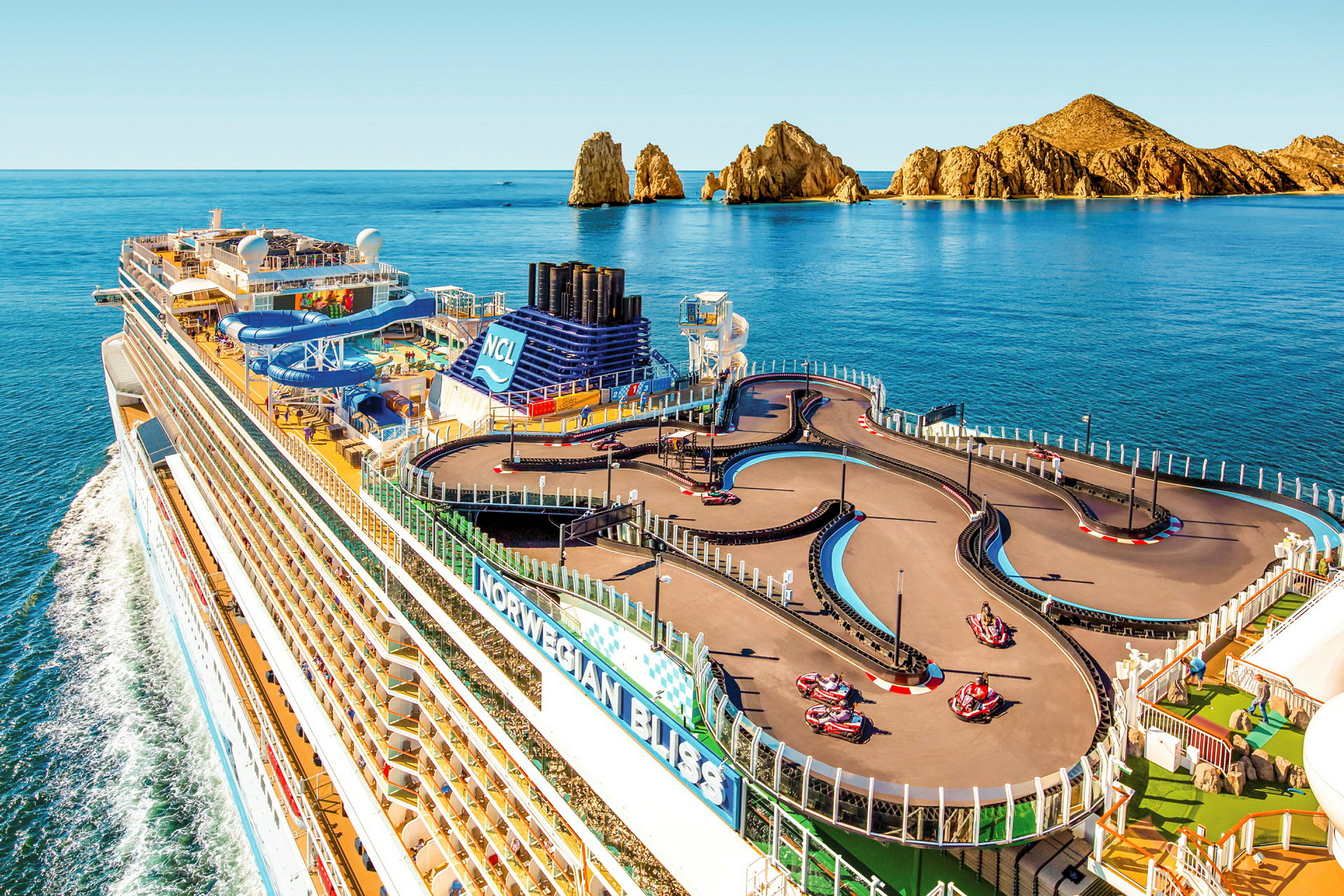 Et cruiseskip med en gokartbane på dekk, omgitt av havet og klippelandskap i bakgrunnen. (AI-generert tekst)