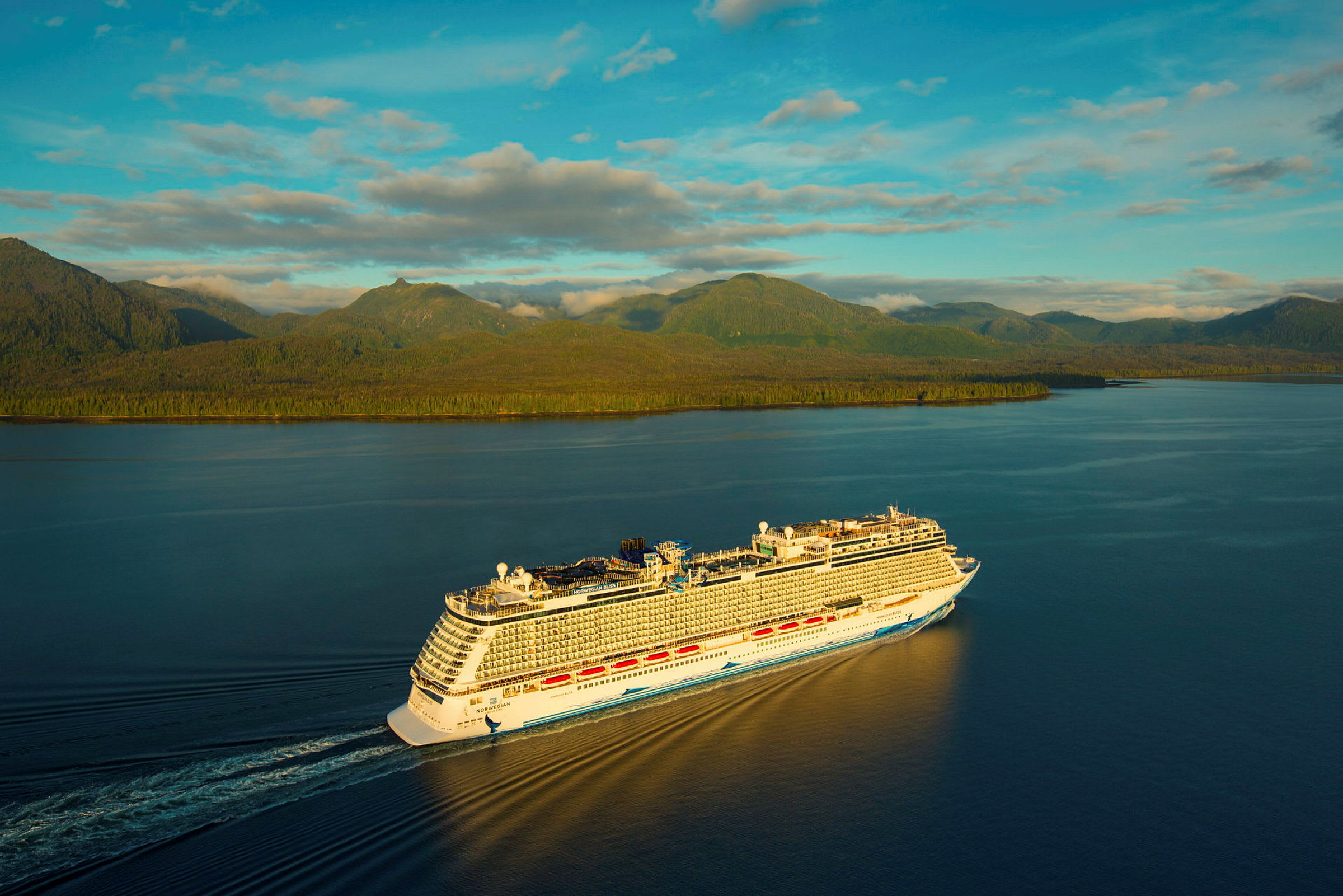 Et cruiseskip seiler på en rolig innsjø med skogkledde fjell i bakgrunnen under en klar himmel. (AI-generert tekst)