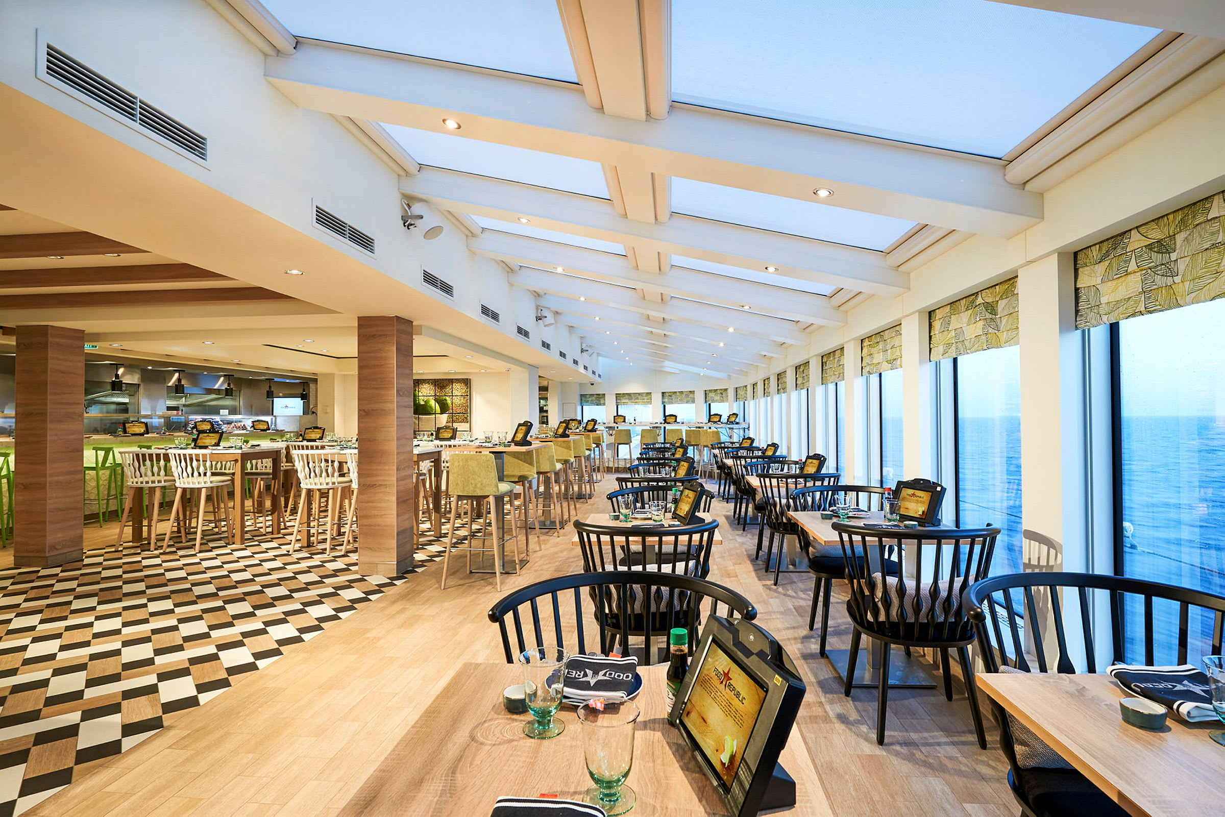 Utsikt over en restaurant med store vinduer og sitteplasser ordnet ved bord. (AI-generert tekst)