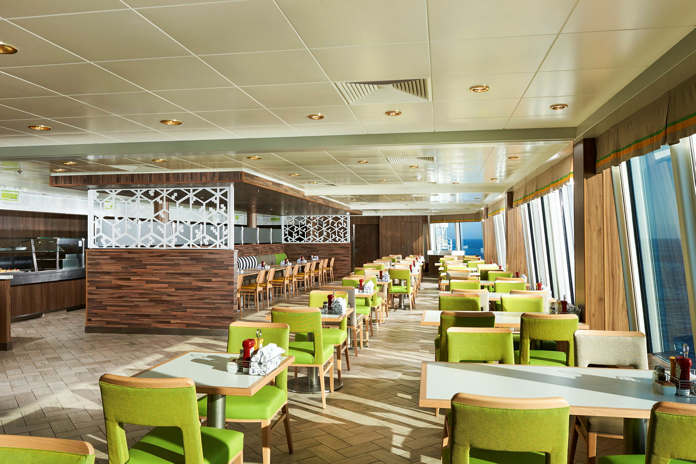 En restaurant med grønnkledde stoler og bord plassert i rekker, med vinduer som viser havet utenfor. (AI-generert tekst)