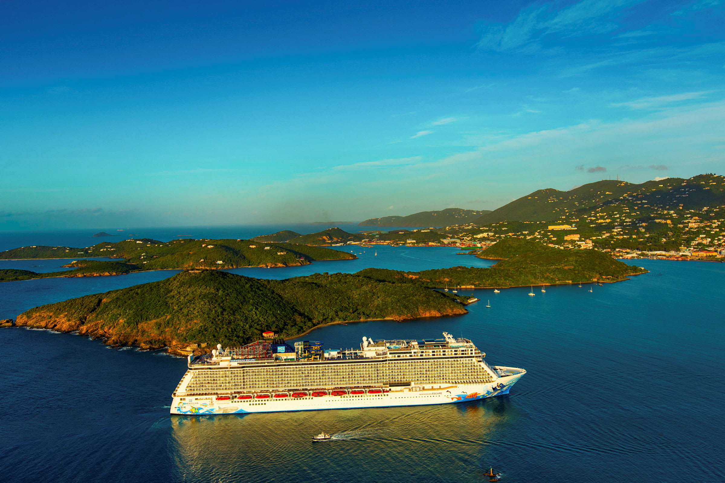 Bilde av et cruiseskip som ligget i en havbukt omgitt av grønne øyer under en klar blå himmel. (AI-generert tekst)