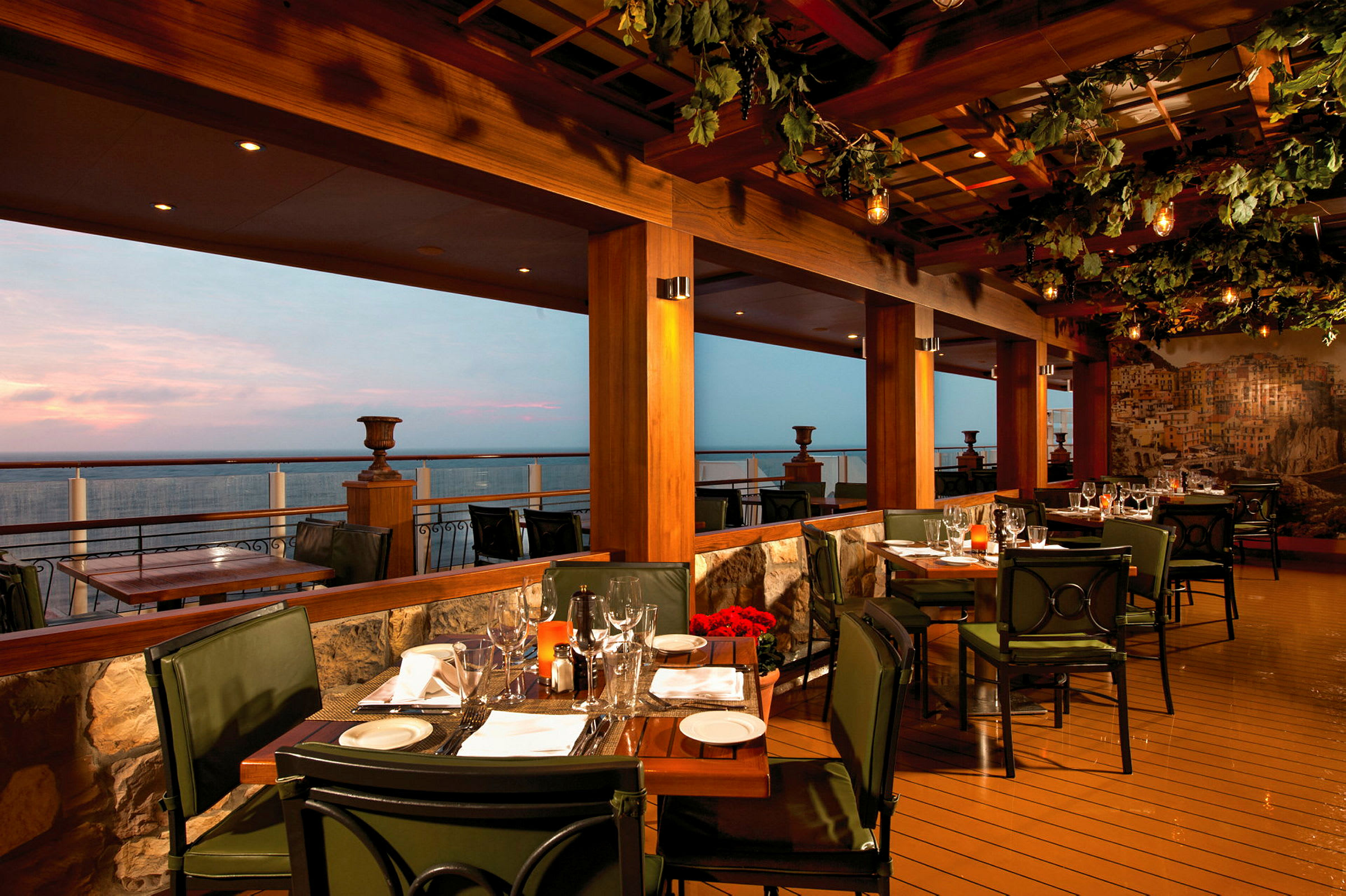 En restaurant med bord og stoler på en terrasse mot havet ved skumringstid. (AI-generert tekst)