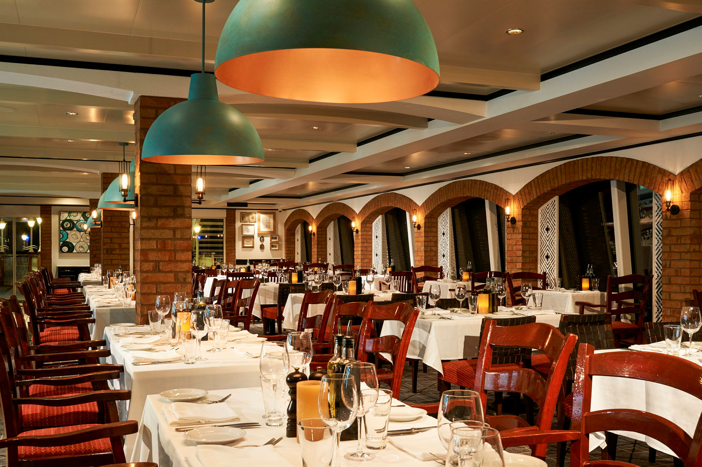 En elegant restaurant med bord dekket med hvite duker og glass, omgitt av teglsteinsvegger og dekorative buer. (AI-generert tekst)