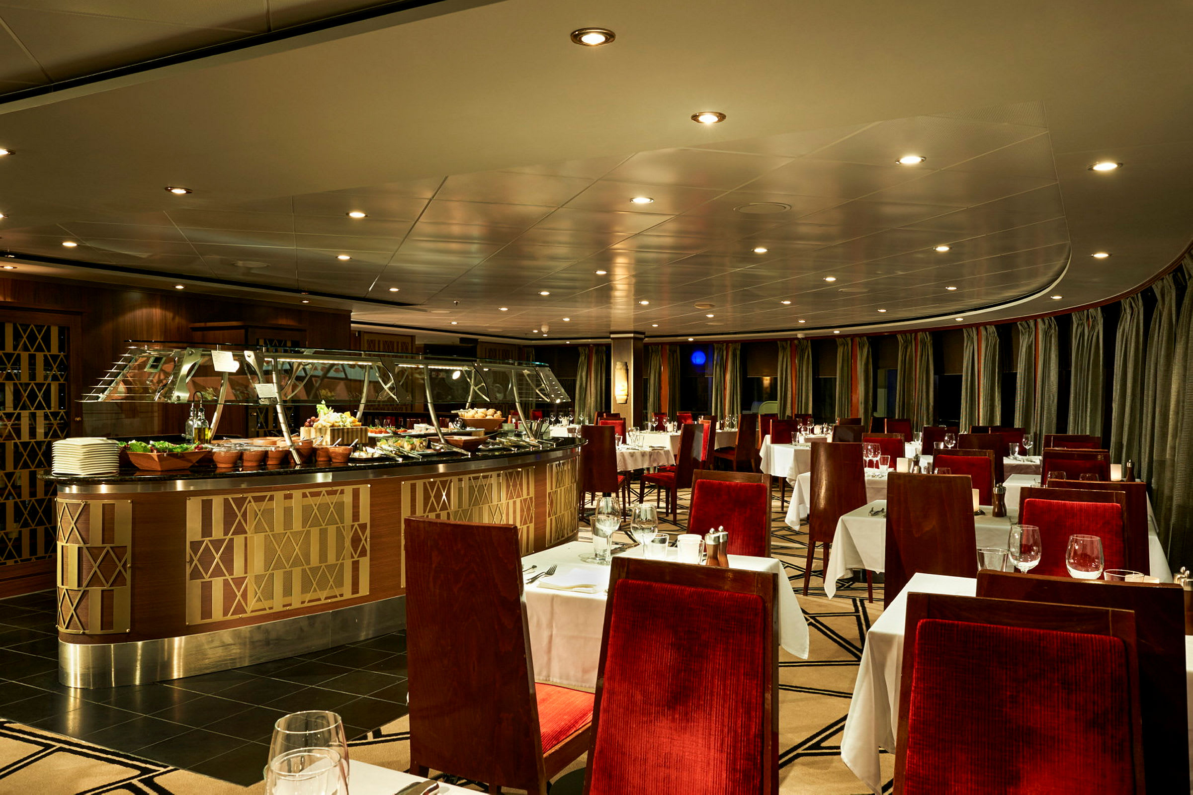 Interiør av en elegant restaurant med røde stoppede stoler og hvite duker. En buffet med mat er plassert i midten. (AI-generert tekst)