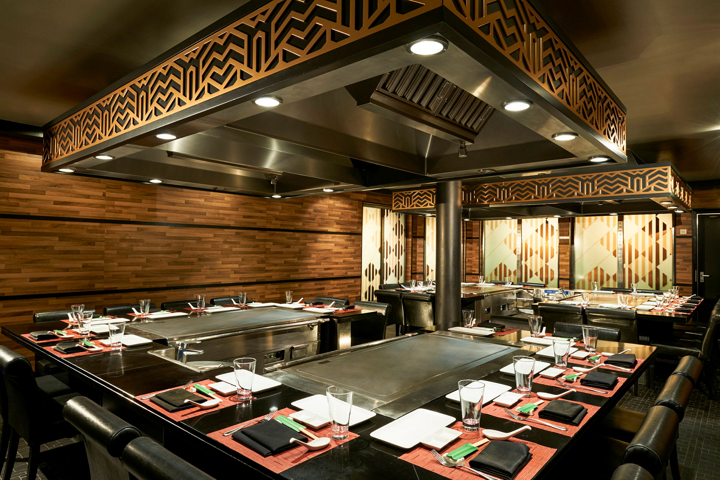 Et teppanyaki-restaurantbord med elegant oppdekking, omgitt av trepaneler og belysning. (AI-generert tekst)