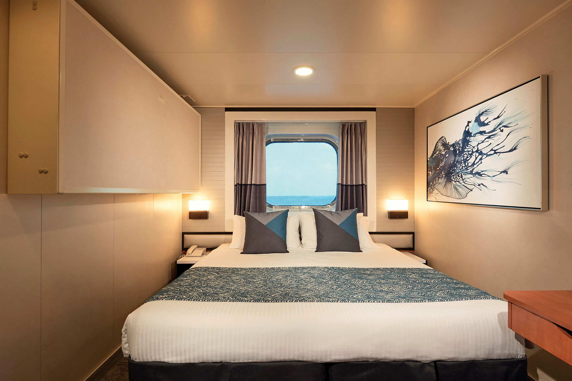 Et hotellrom med en seng, kunst på veggen og et vindu med utsikt over havet. (AI-generert tekst)