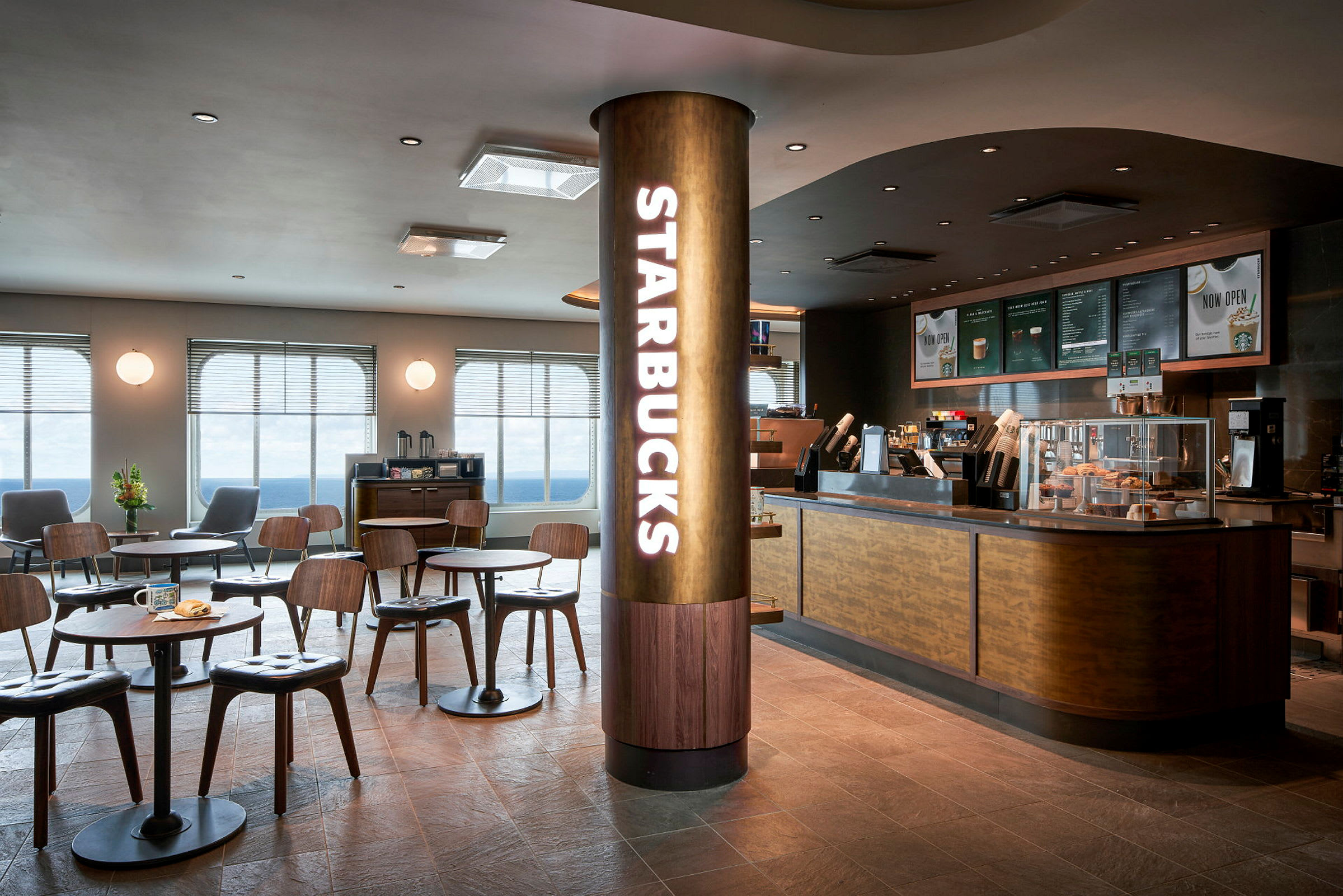 Et moderne kafé med Starbucks-logo på en søyle og sitteplasser med bord foran en serveringsdisk. (AI-generert tekst)